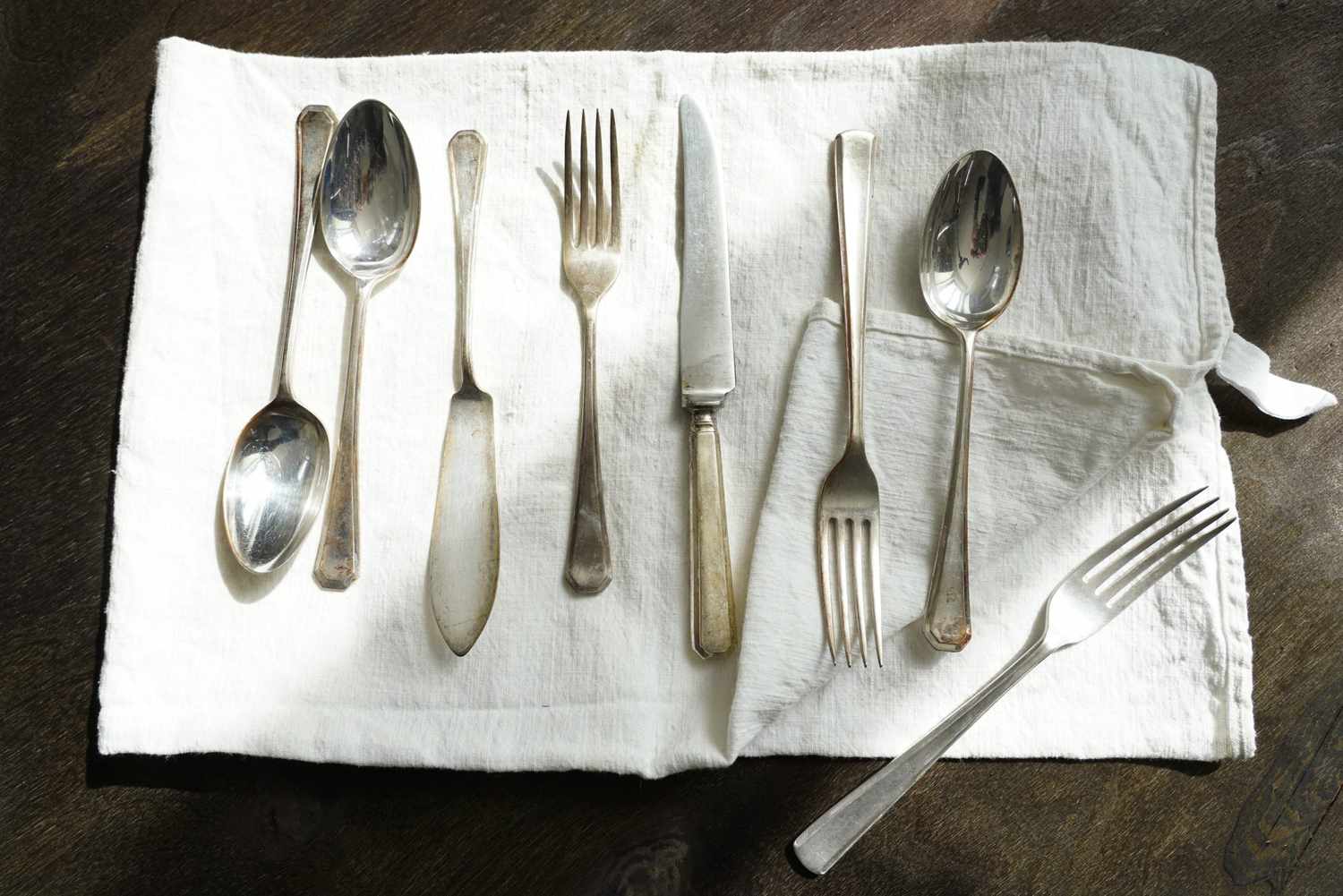Set of Vintage English Silver Cutlery over an Old Linen Cloth and a Dark Wooden Background. Top View