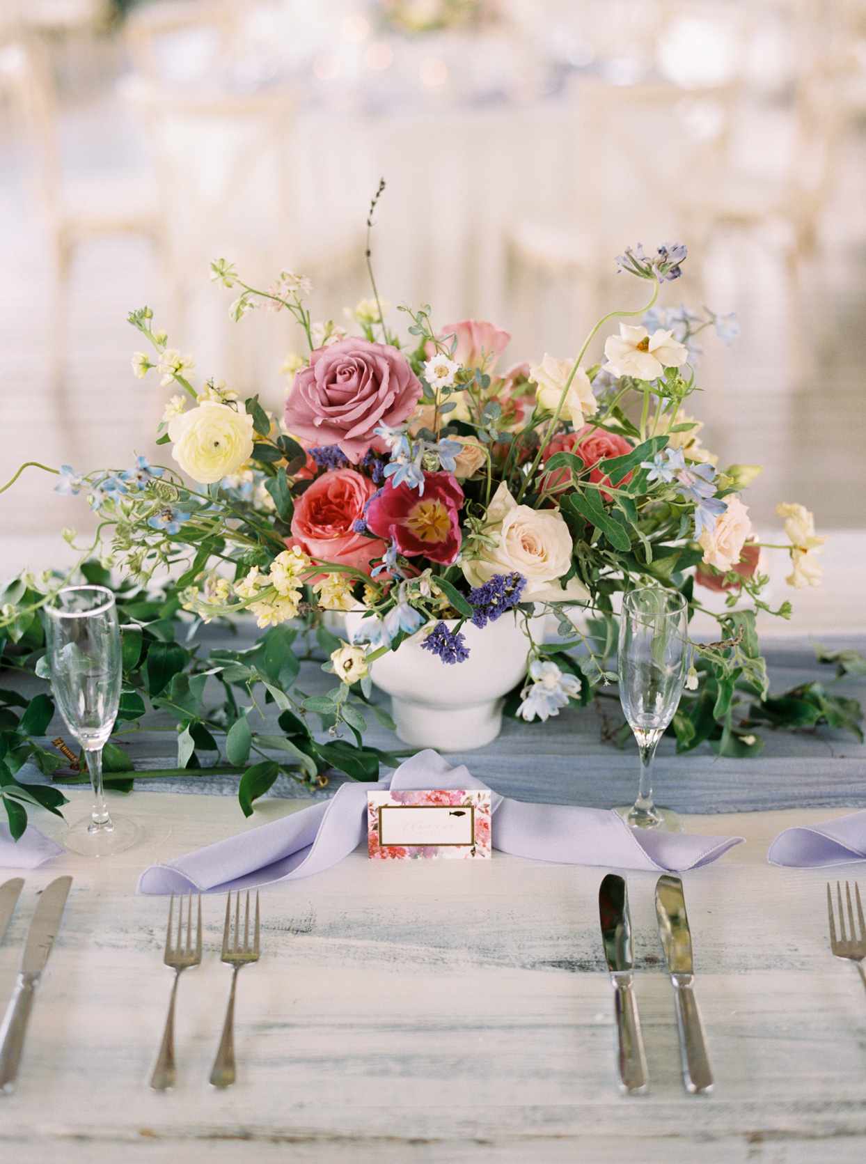 wedding reception tablescape with flowers in low white vessels and lavender napkins
