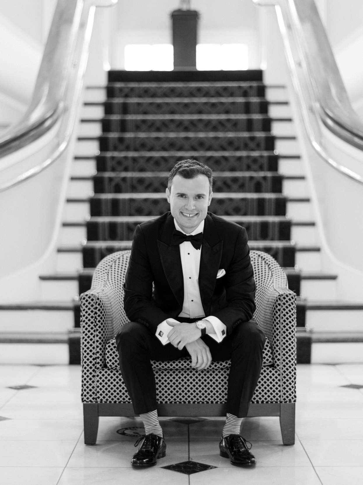 groom sitting in chair wearing black and white classic tux