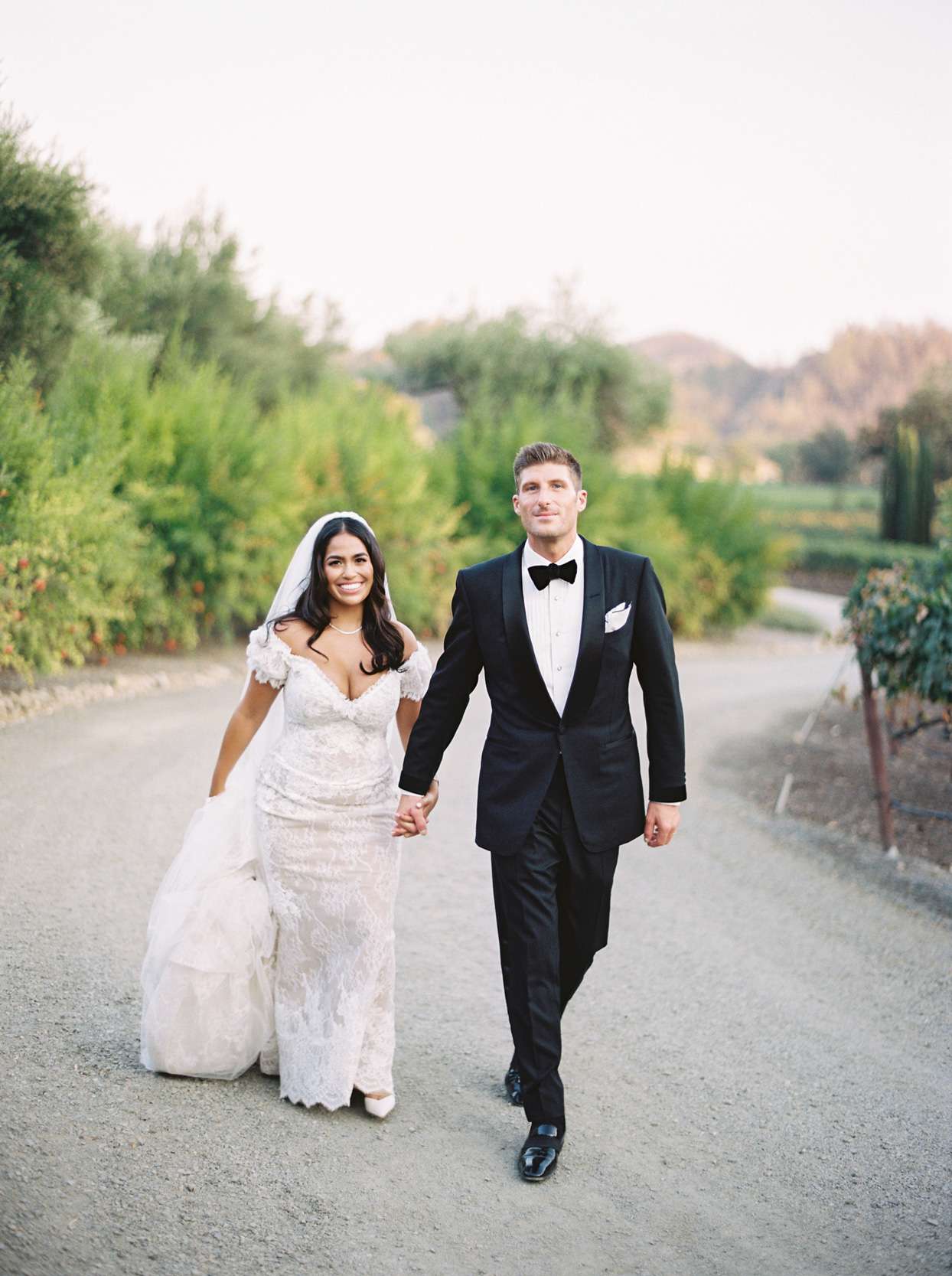 bride and groom smiling holding hands walking on gravel road