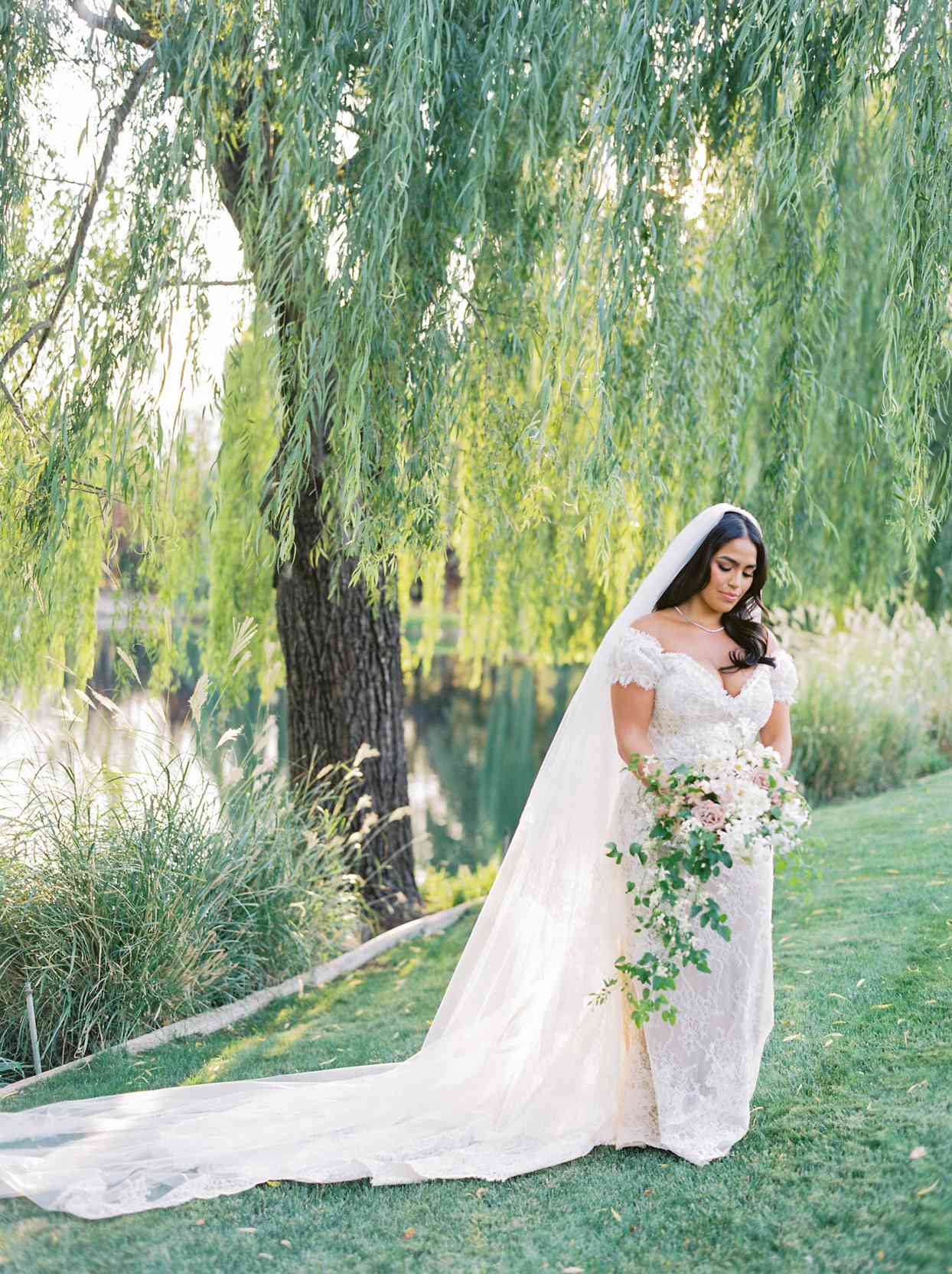 bride standing under willow tree outside holding bouquet