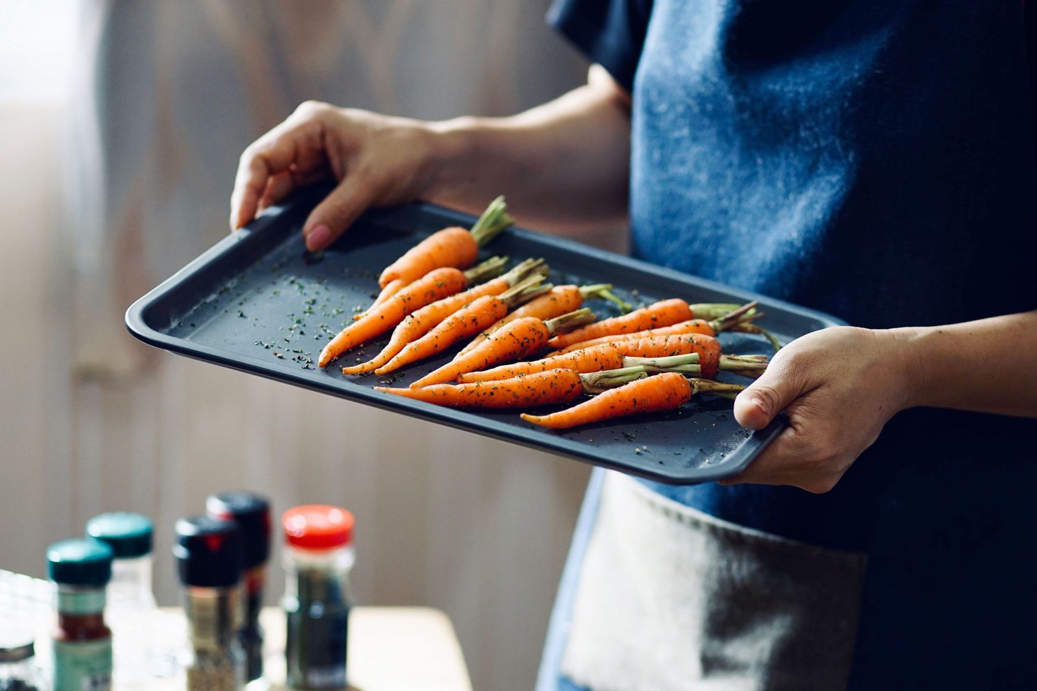 mid section of woman holding roasting pan with carrots