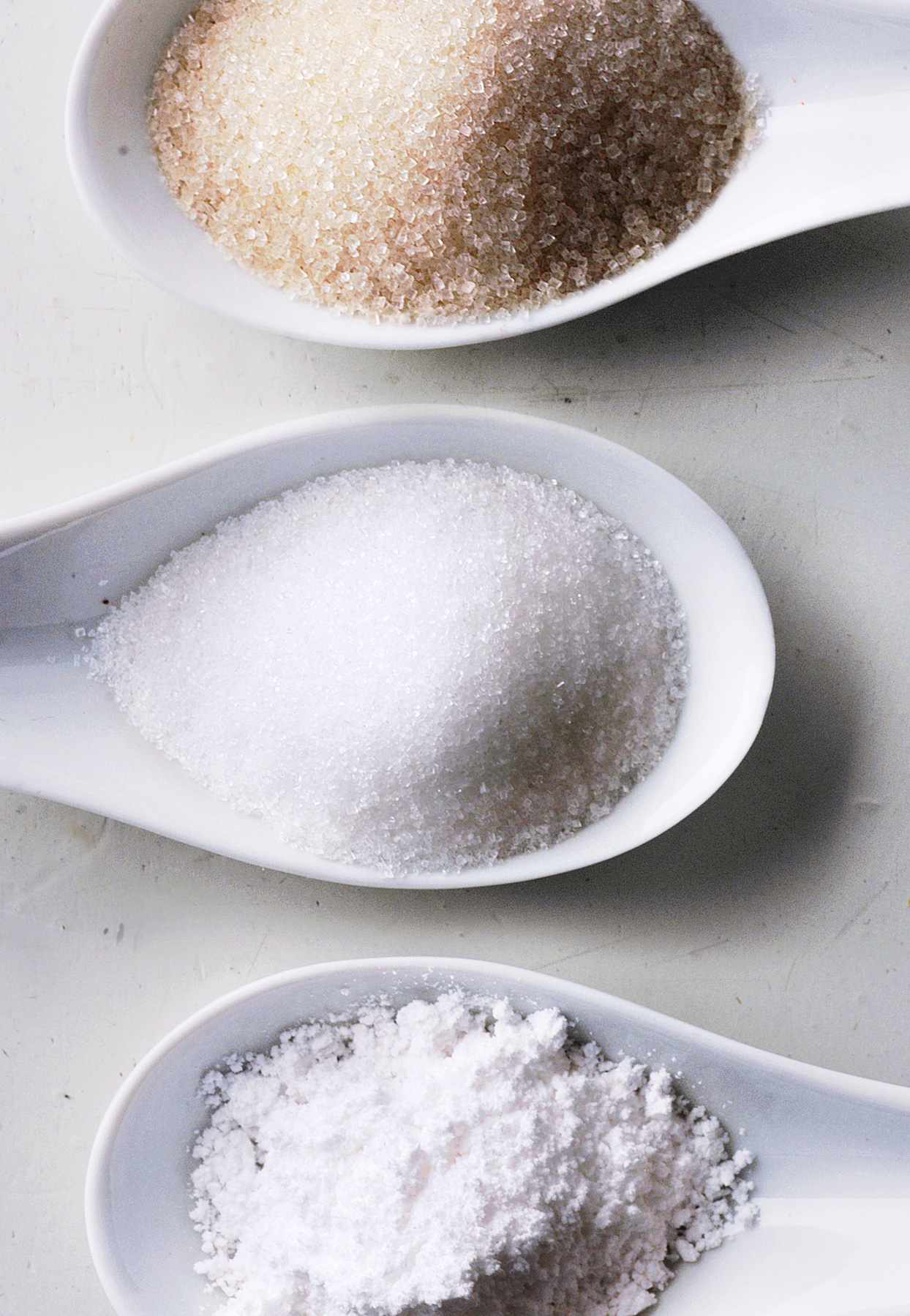 three white spoons of different sugars