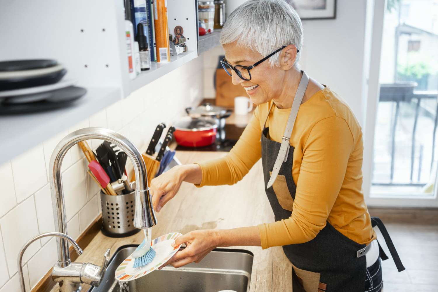 senior woman washing dishes in sink