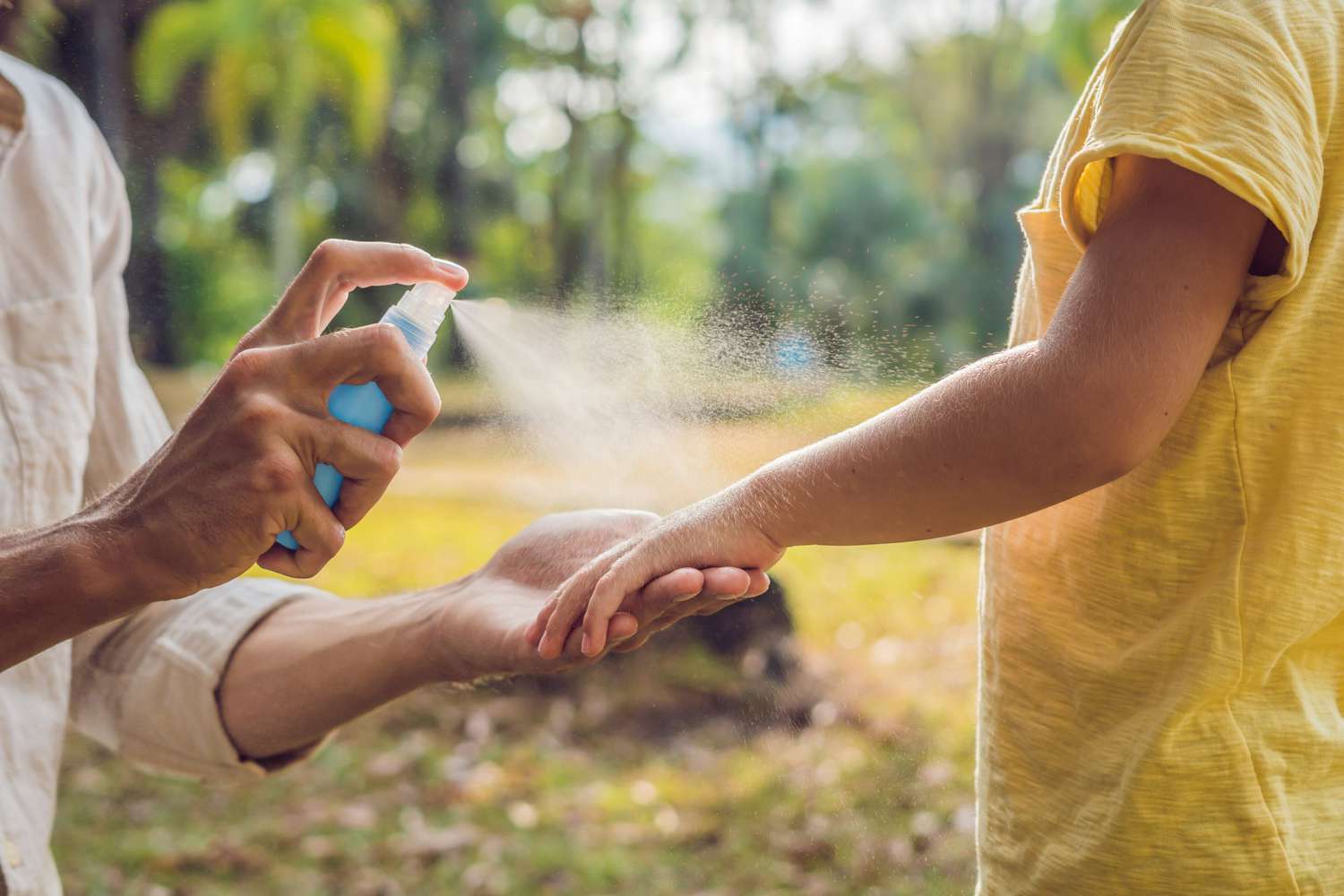 mother spraying bug spray on child's arms outdoors