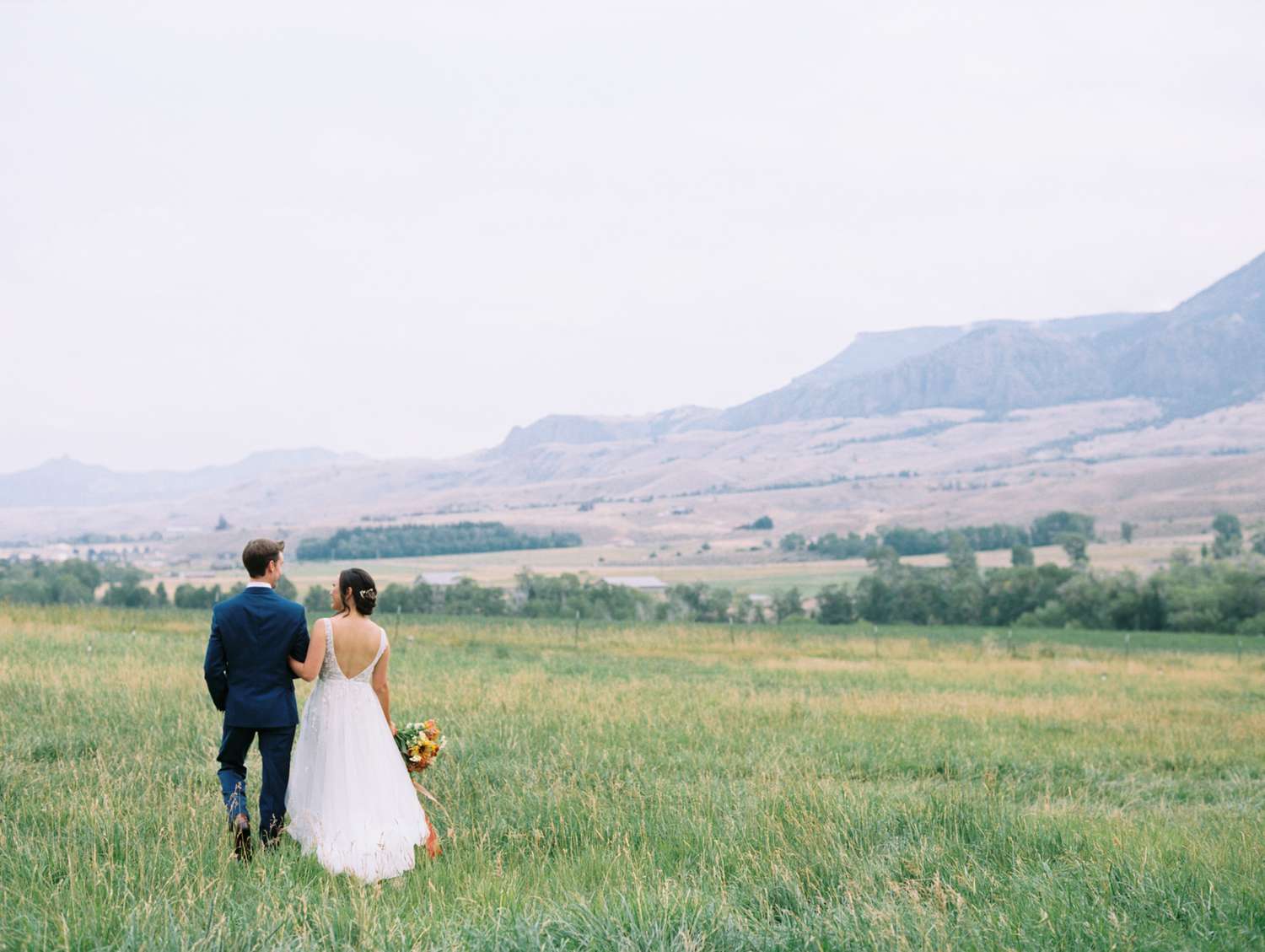 bride and groom walking in the grass overlooking mountains