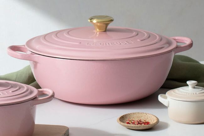 Pink and white Le Creuset cookware products on table