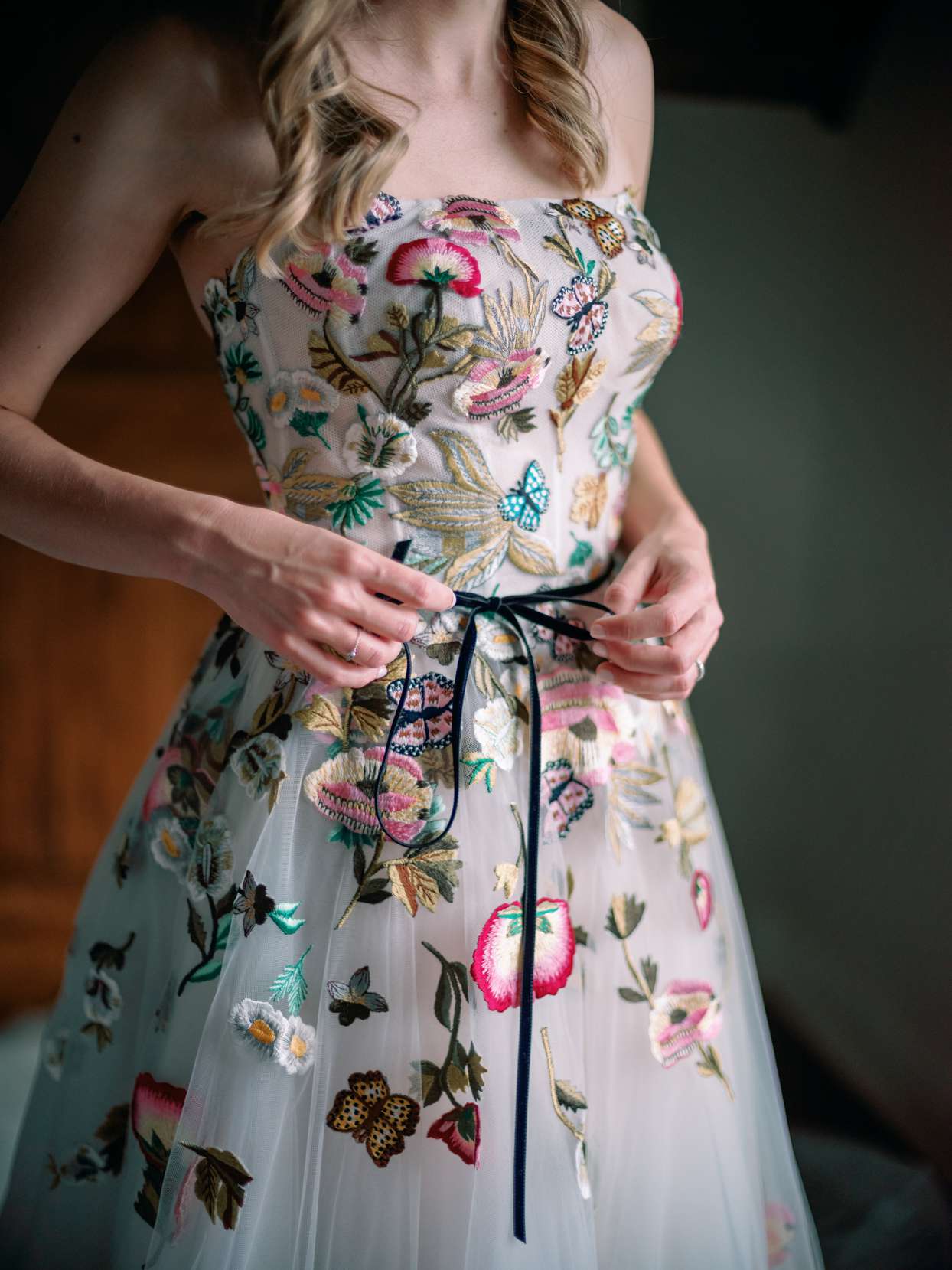 bride tying bow around wedding dress with floral embroidery