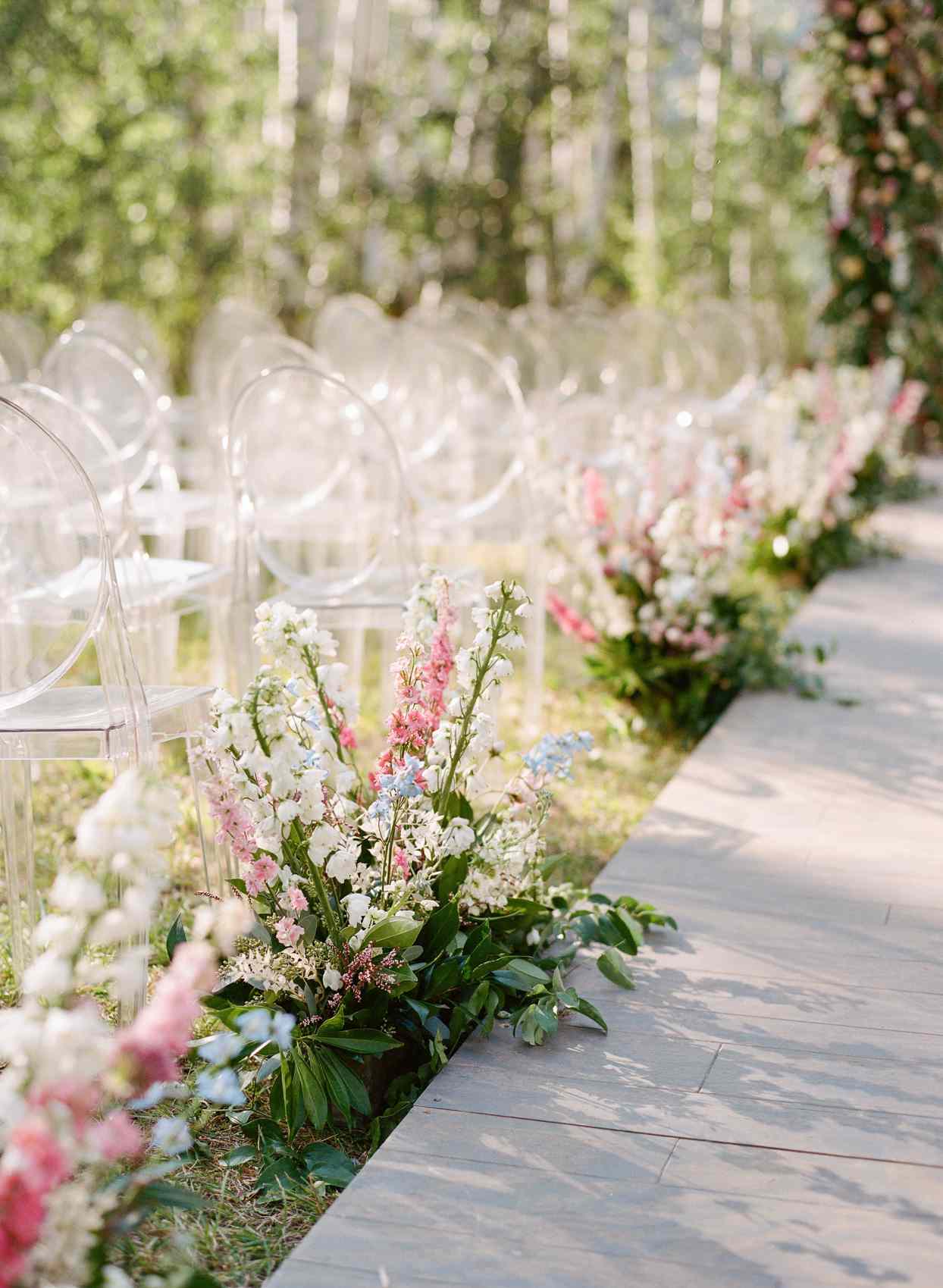 ghost chairs and wildflower arrangements with tall stems lining aisle