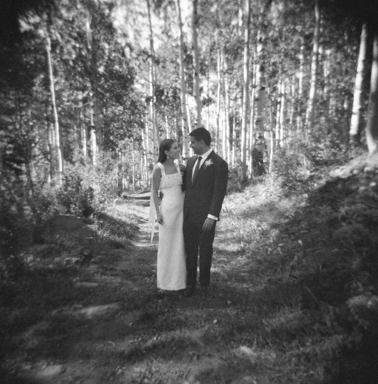 black and white image of bride and groom on path lined with aspen trees
