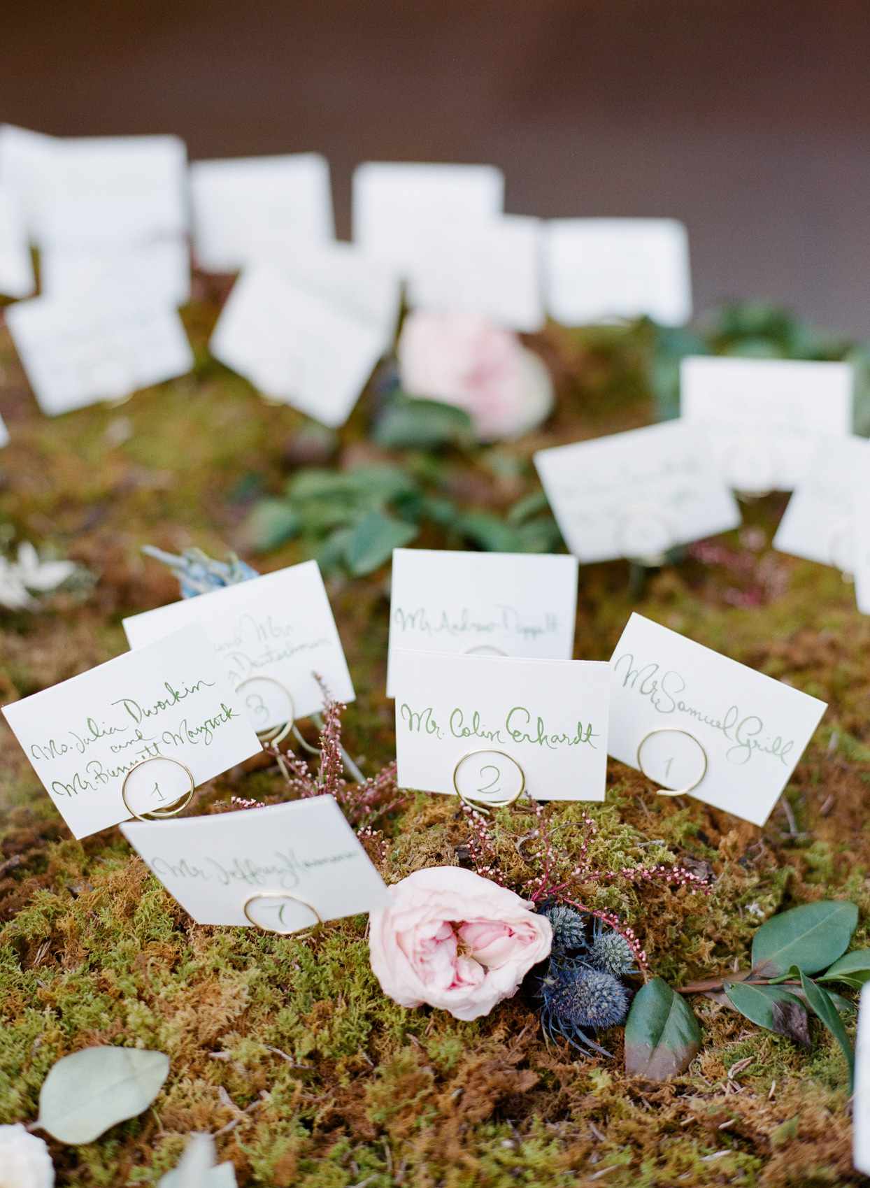 escort cards displayed on bed of moss with floral embellishments