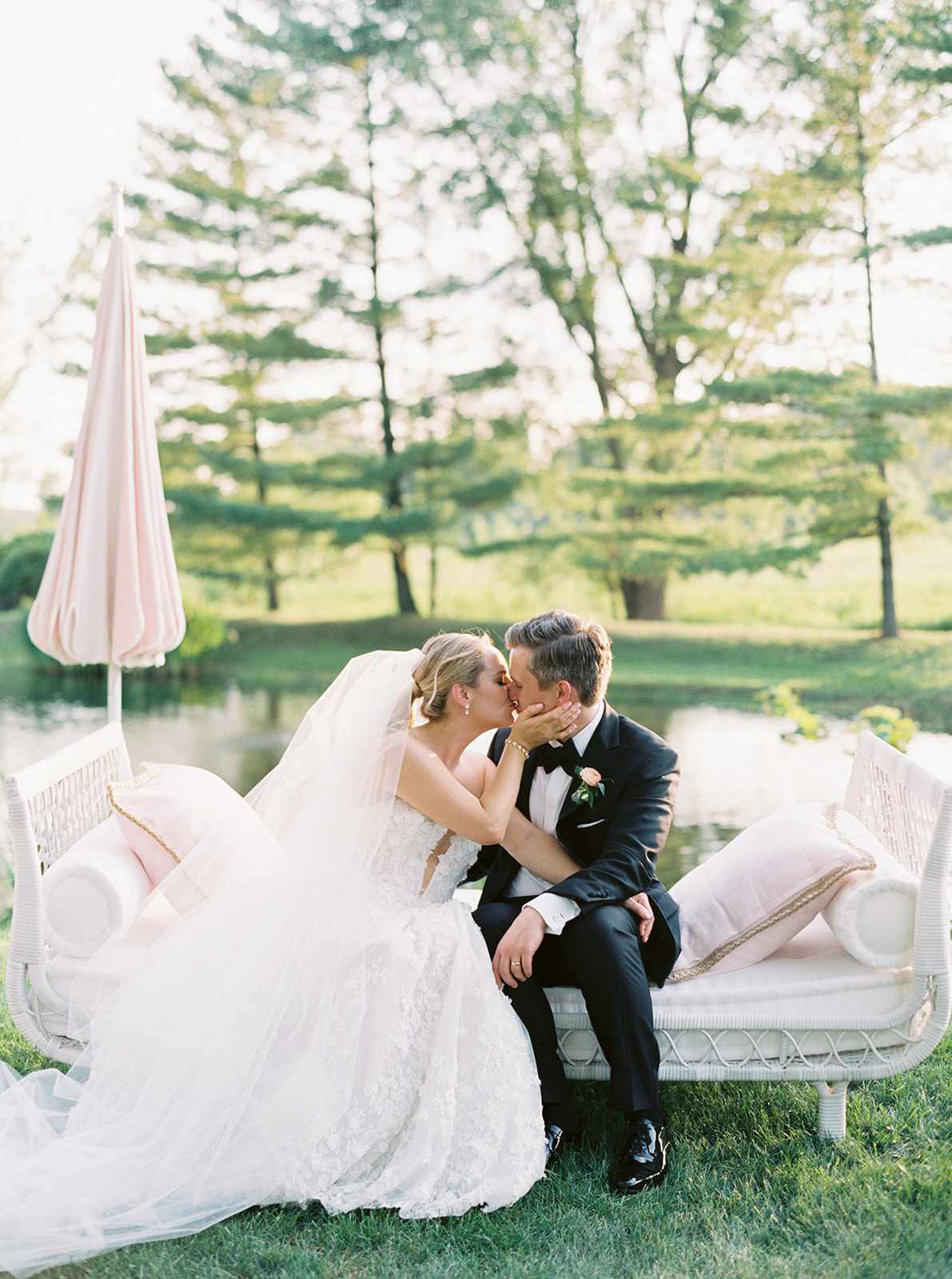 bride and groom sharing a kiss sitting on white outdoor bench