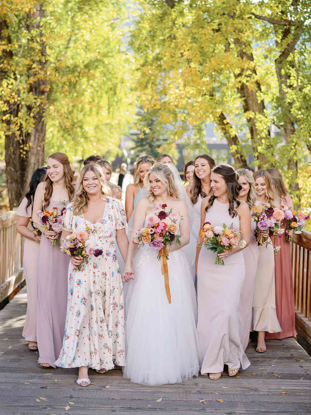 bride with bridesmaids in mismatched dresses walking on bridge
