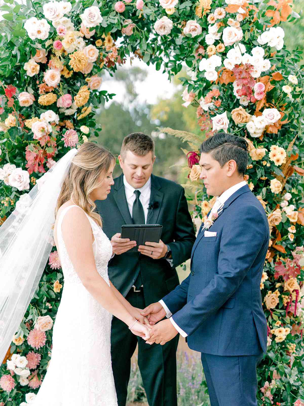 bride and groom exchanging vows beneath floral arch