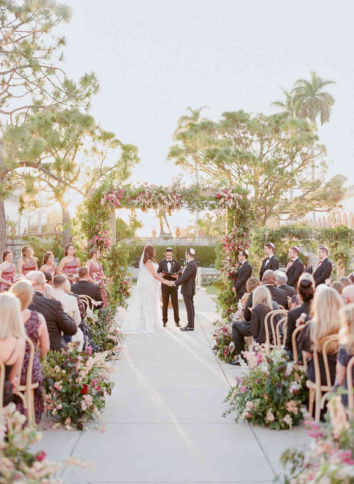 bride and groom under pink floral wedding ceremony chuppah