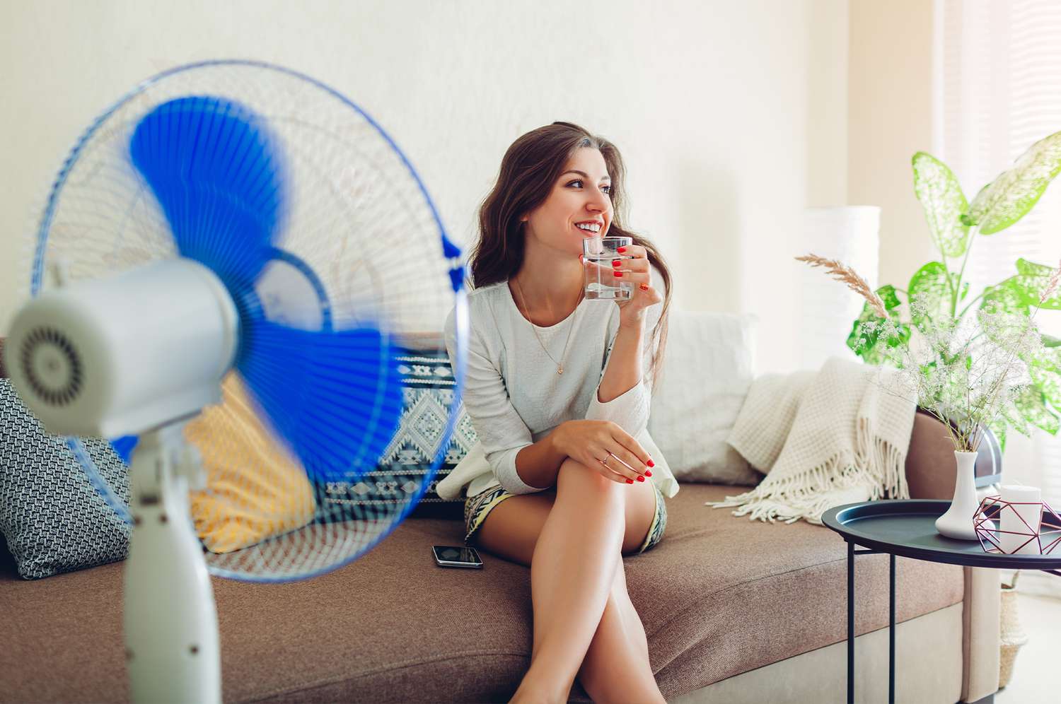 Woman drinking water and sitting in front of electric fan