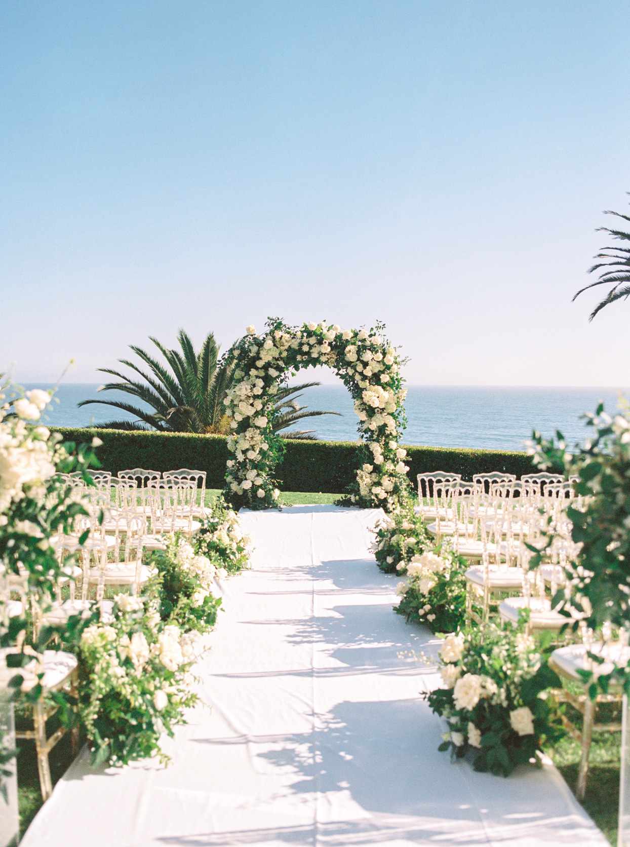 wedding ceremony setup with florals along the aisle and view of the ocean