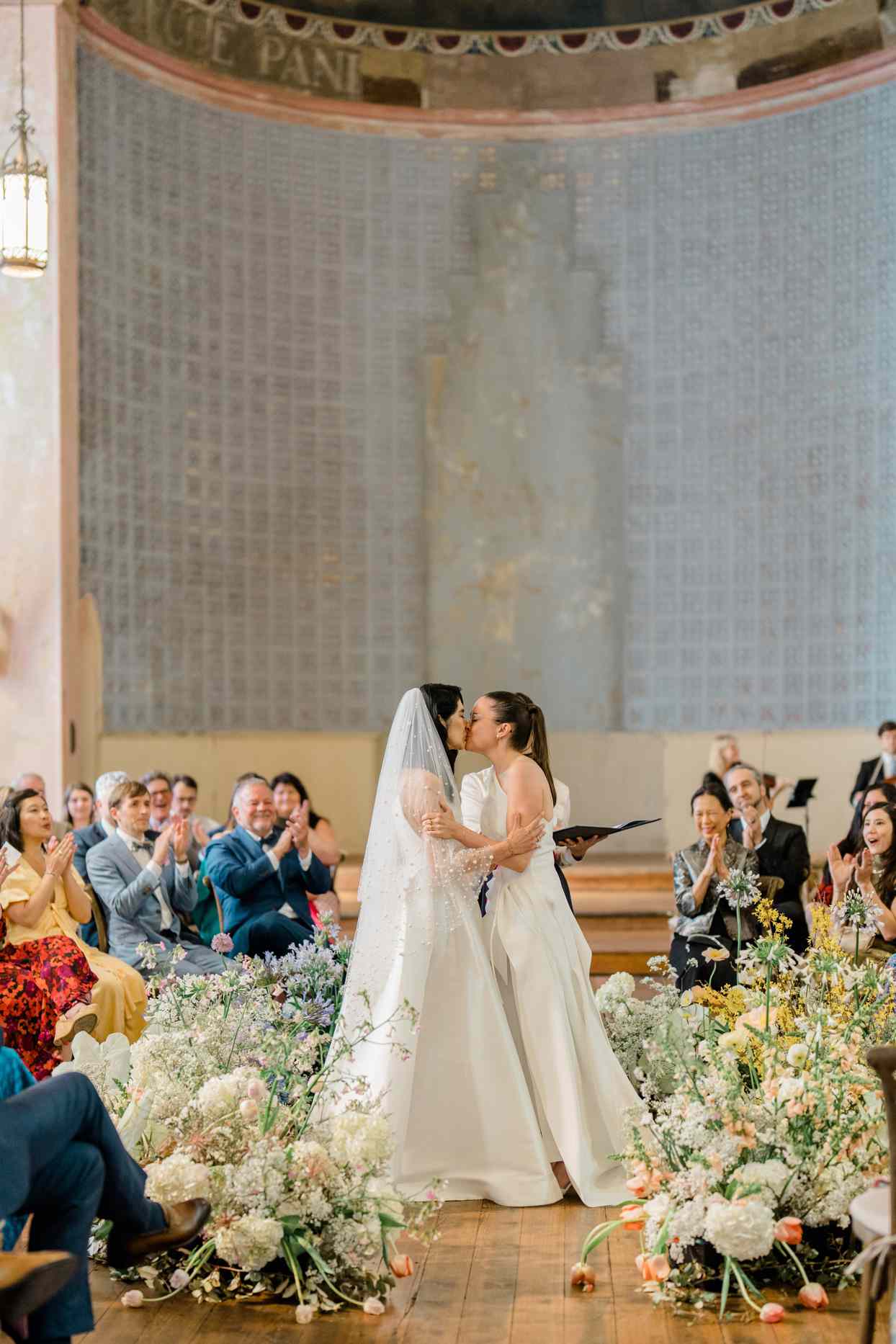 brides kissing at the altar surrounded by guests