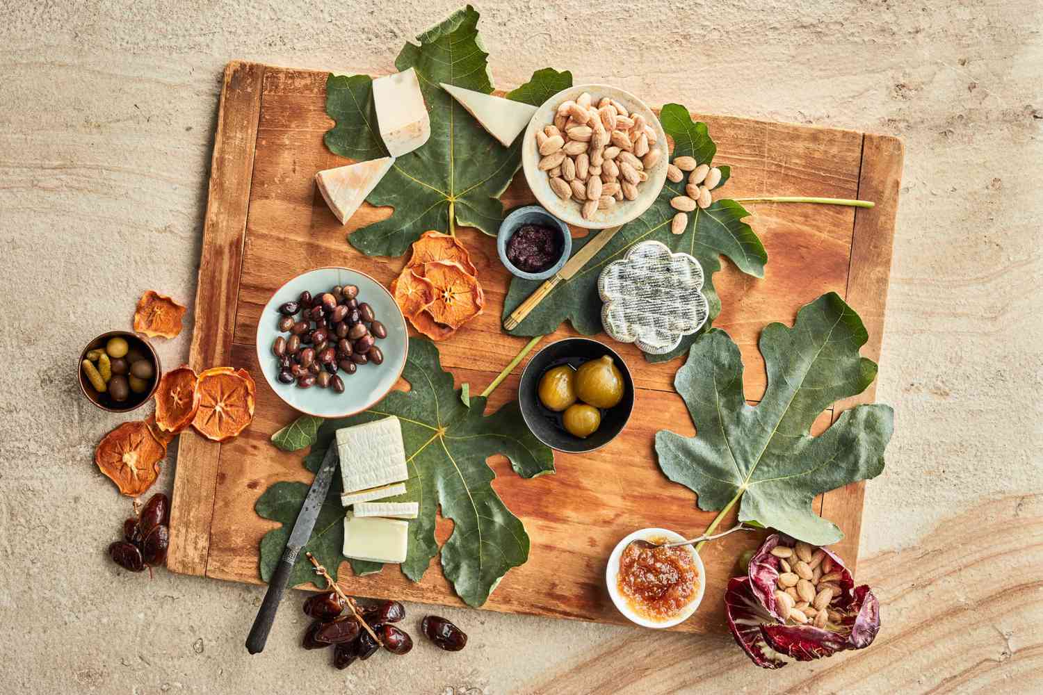 Wooden serving board with leaves, nuts, and olives
