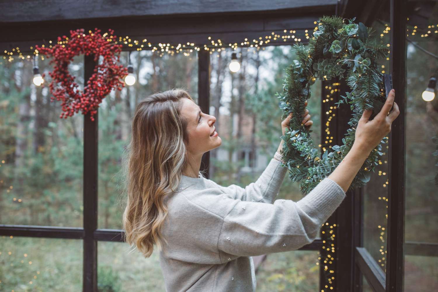 Woman hanging christmas wreaths inside home as christmas decor