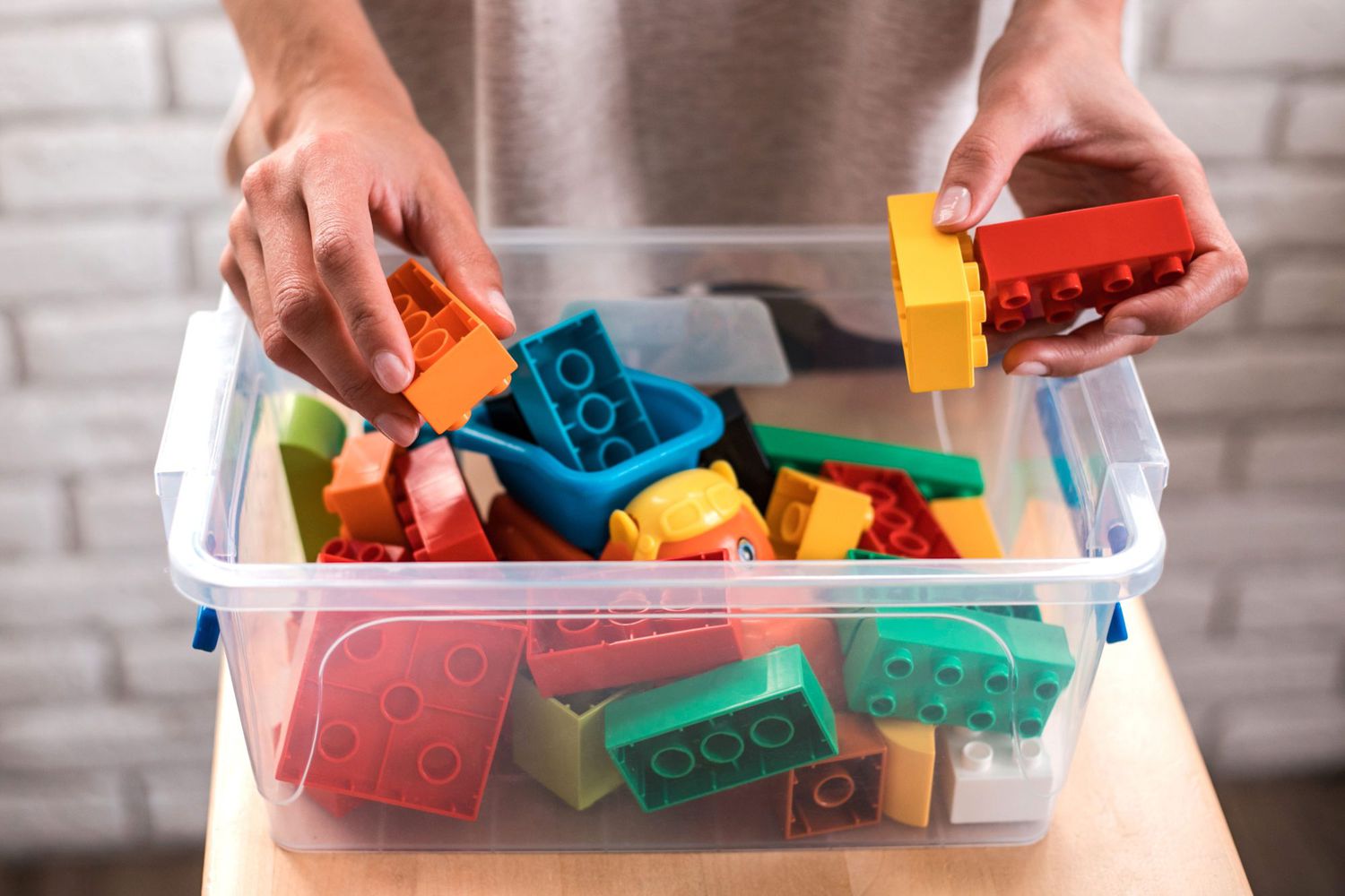 Woman's hands putting colored blocks into plastic box. Close up.