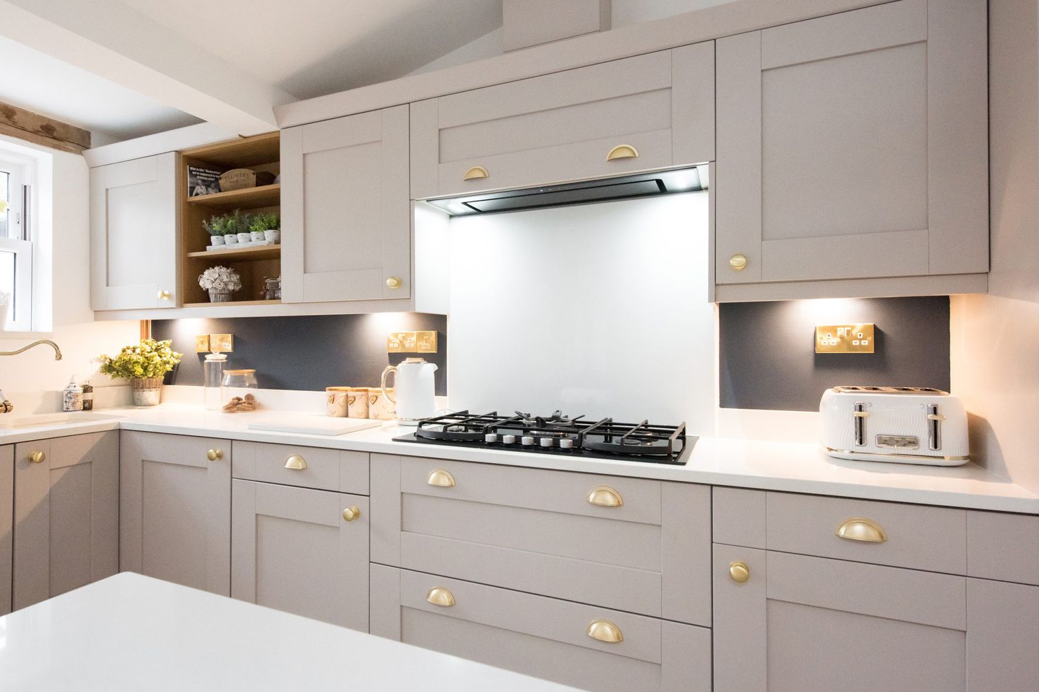 An interior view of a taupe, champagne coloured fitted kitchen diner with gold handles, quartz island, gas stove, toaster