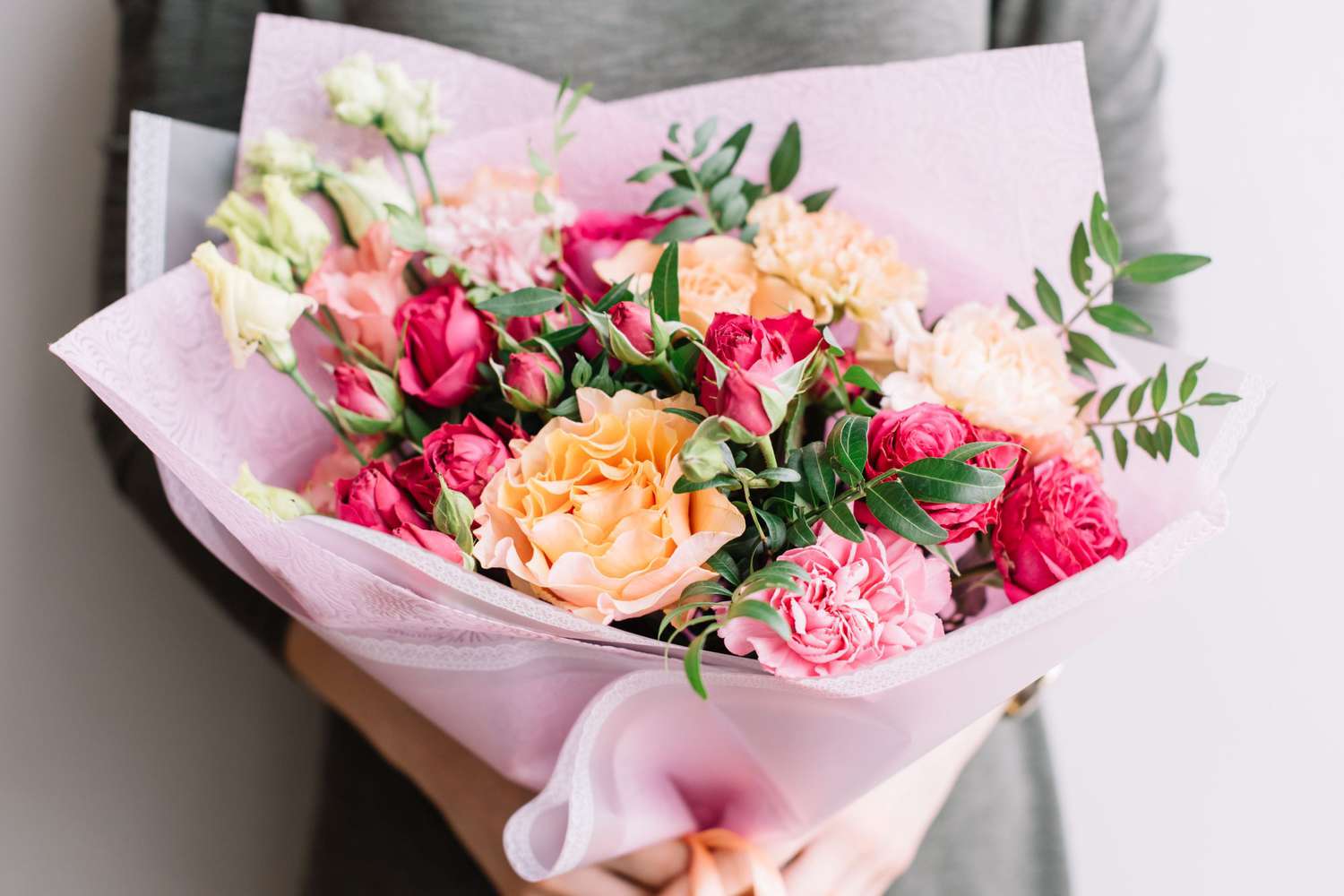 woman holding a colourful fresh blossoming flower bouquet of different sorts of roses, carnations, eustoma, peonies