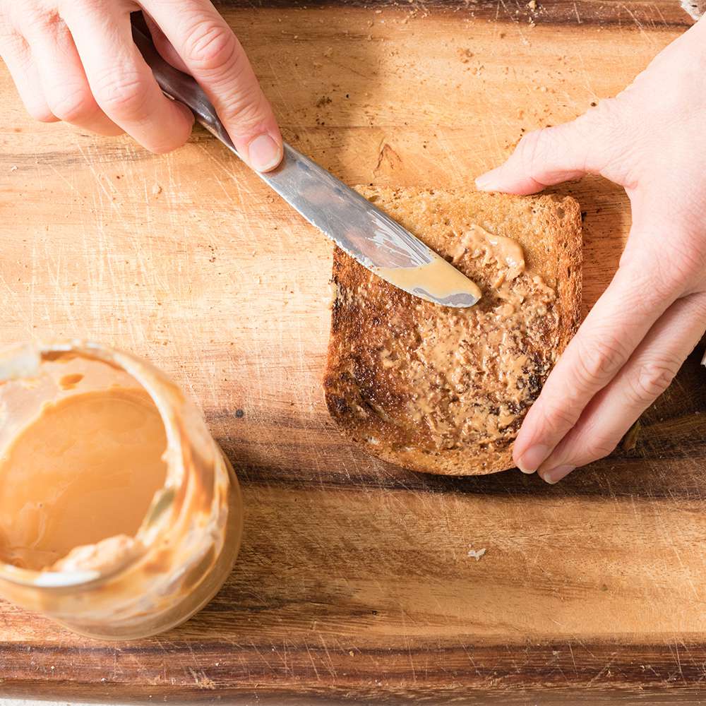 woman making peanut butter toast metabolism boosting food