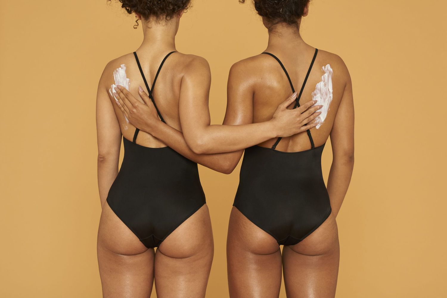 The Best Sunscreens for Darker Skin Tones , Two women applying suncream to each others back