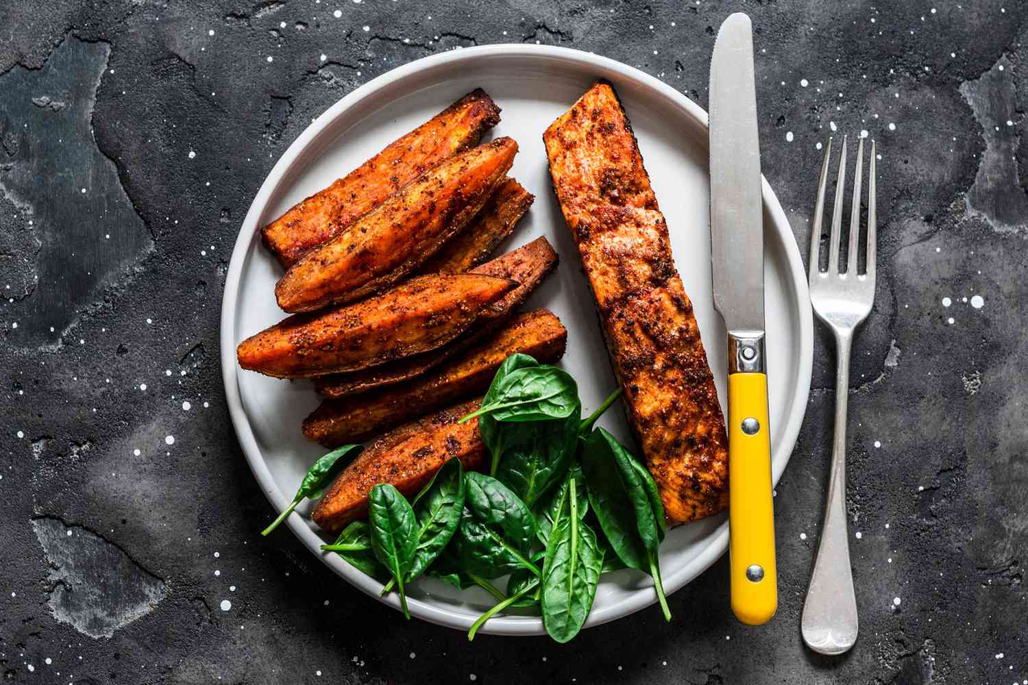Crispy spice crust baked salmon with sweet potato and spinach - healthy balanced lunch on dark background, top view