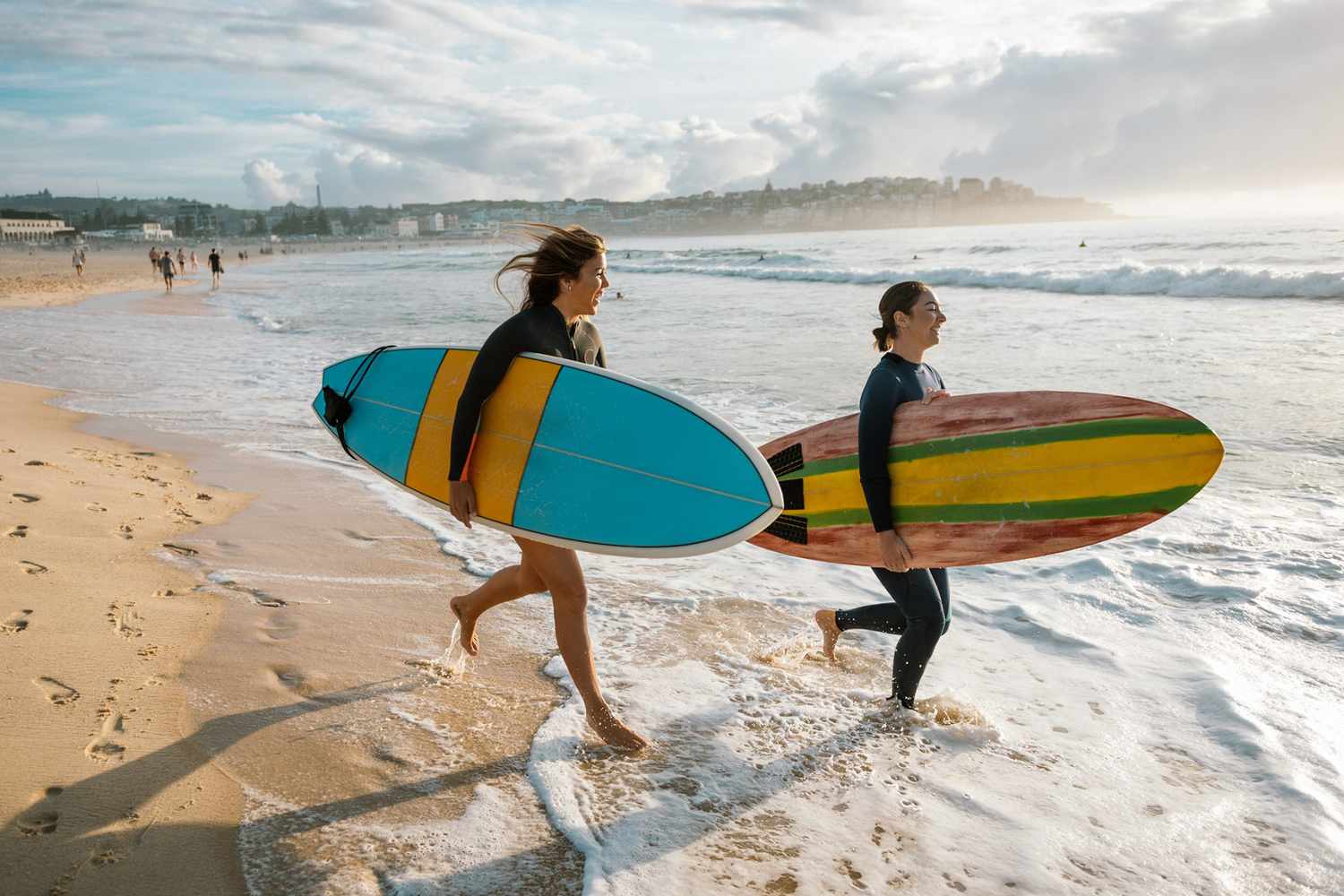 Two women running into the ocean with surfboards