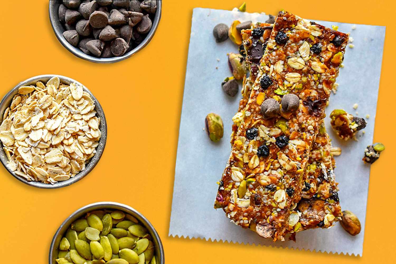 Overhead shot of homemade granola bars on parchment paper, surrounded by pistachios, oats, raisins and chocolate chips on an orange background