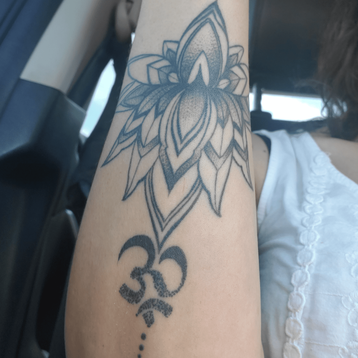 woman in car with large lotus ohm tattoo on arm