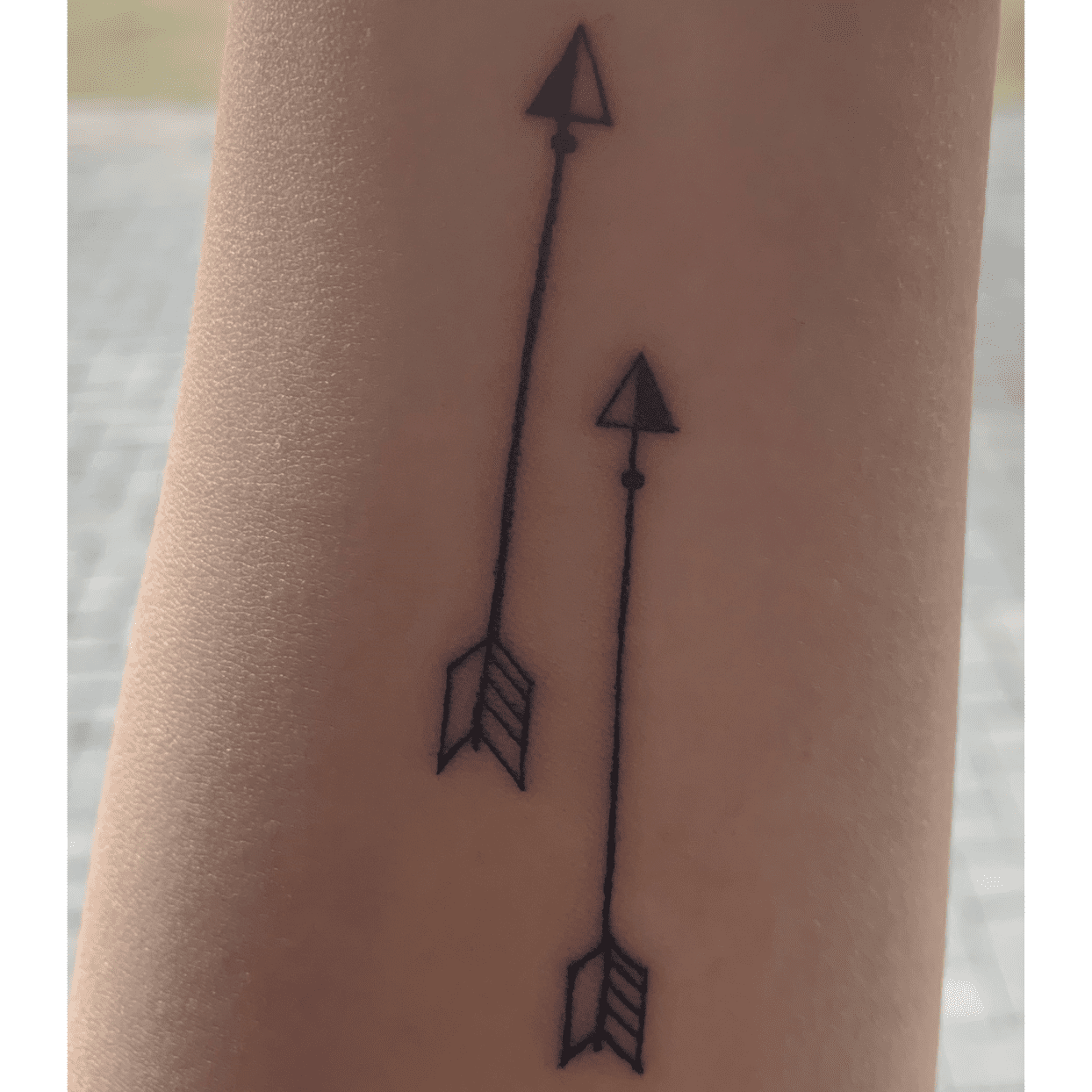 female wrist with two arrow tattoos pointing forward