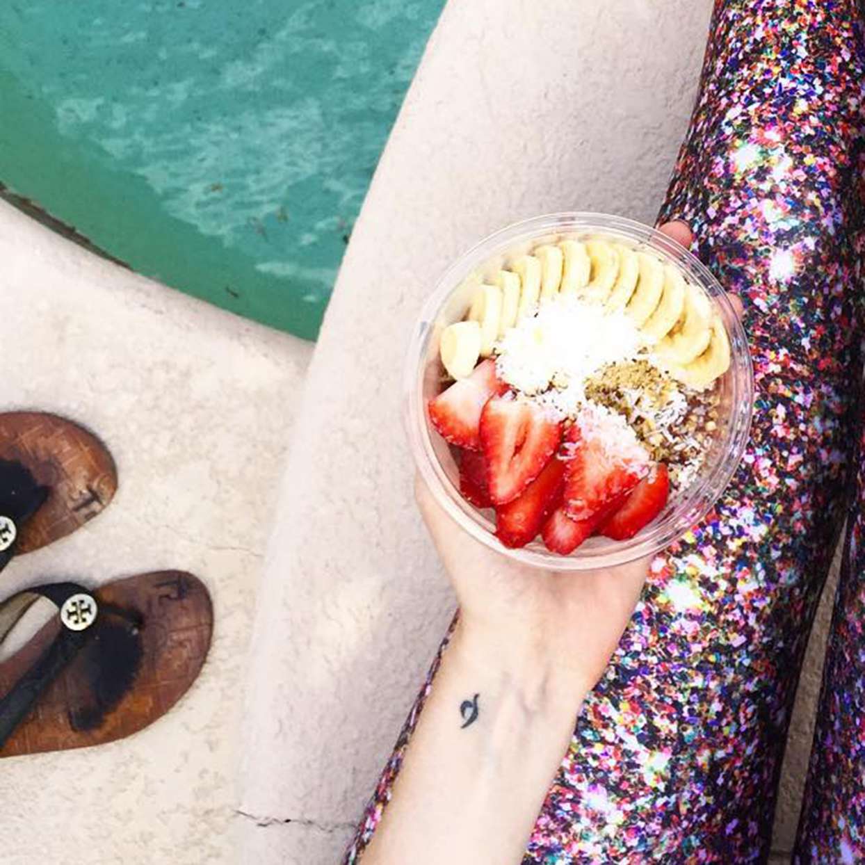 Hand holding acai bowl with small tattoo on wrist