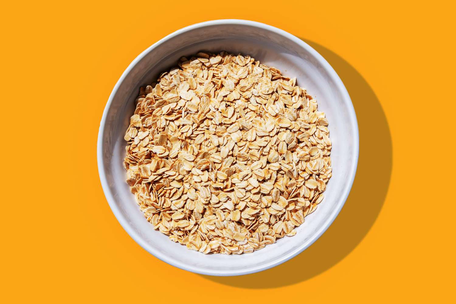 Bowl of dried oats on an orange background