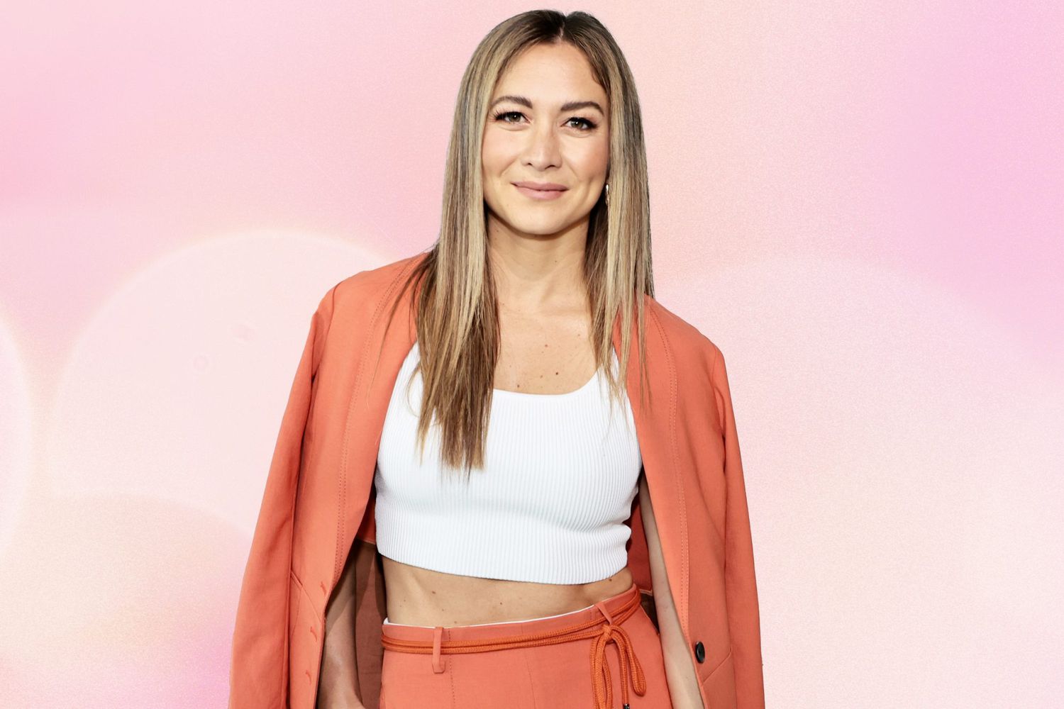 Emma Lovewell wearing a peach blazer and pant against a pink background