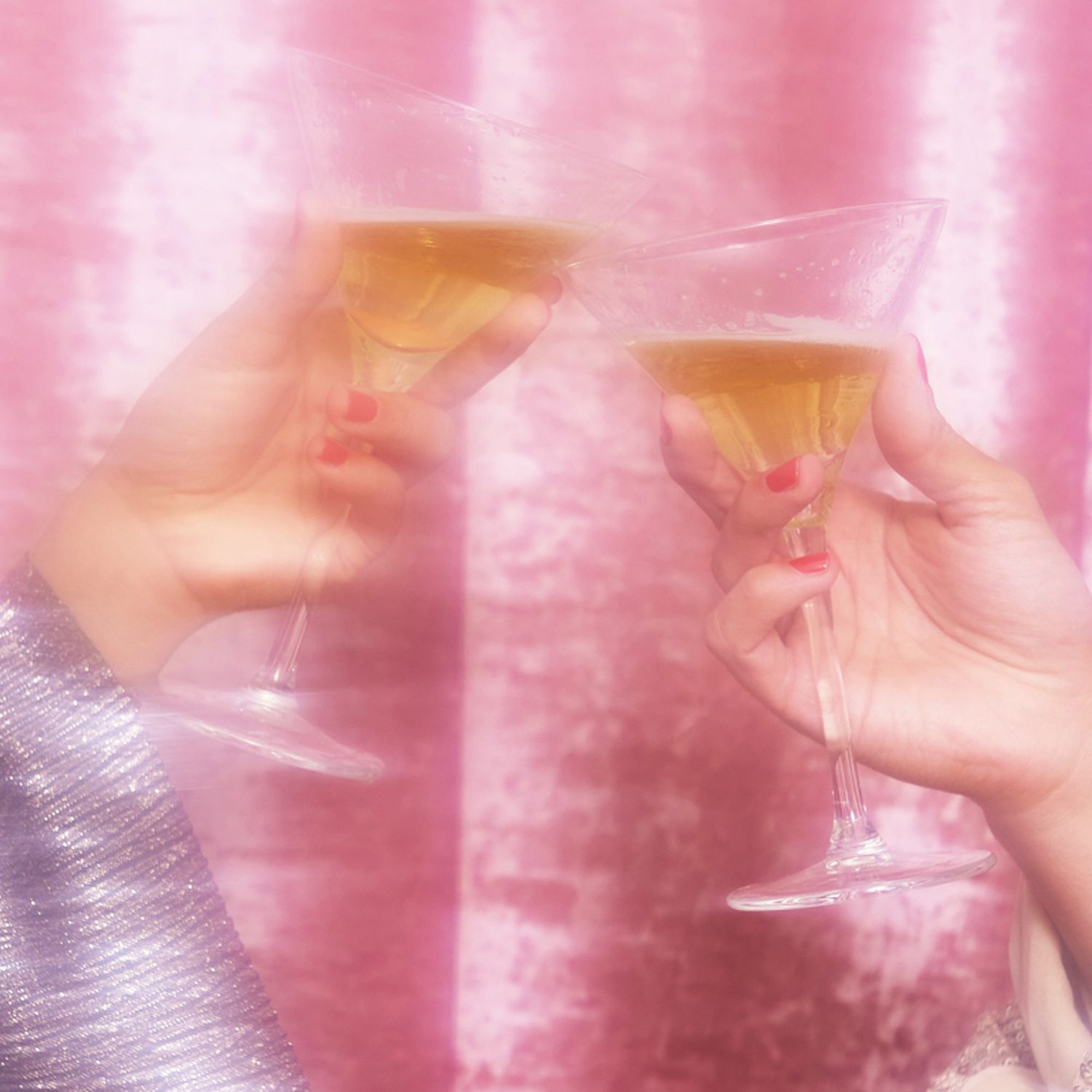 glowy and hazy image of two hands toasting champagne against a pink background