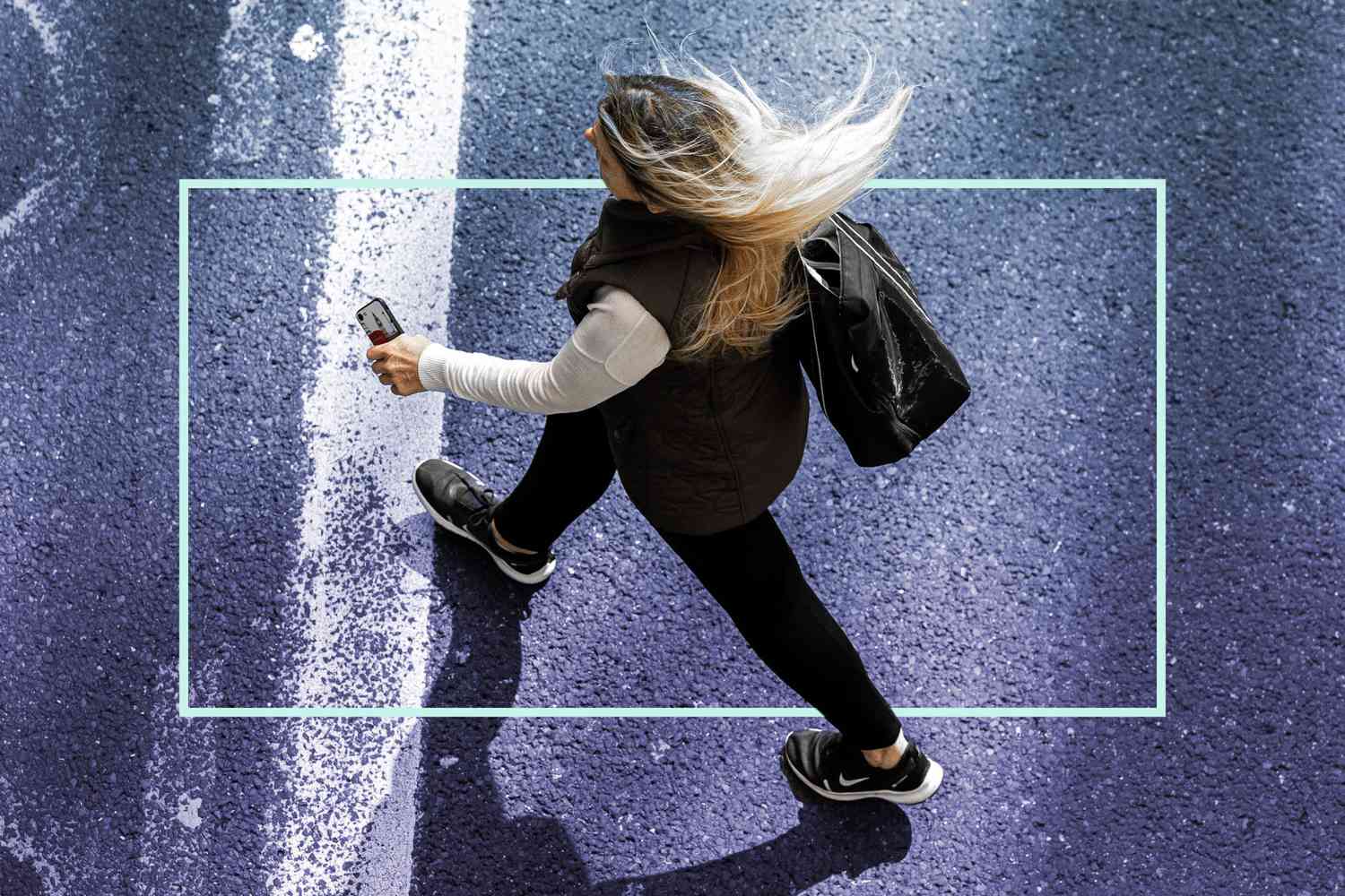 overhead shot of a woman walking across the street, holding her phone in one hand