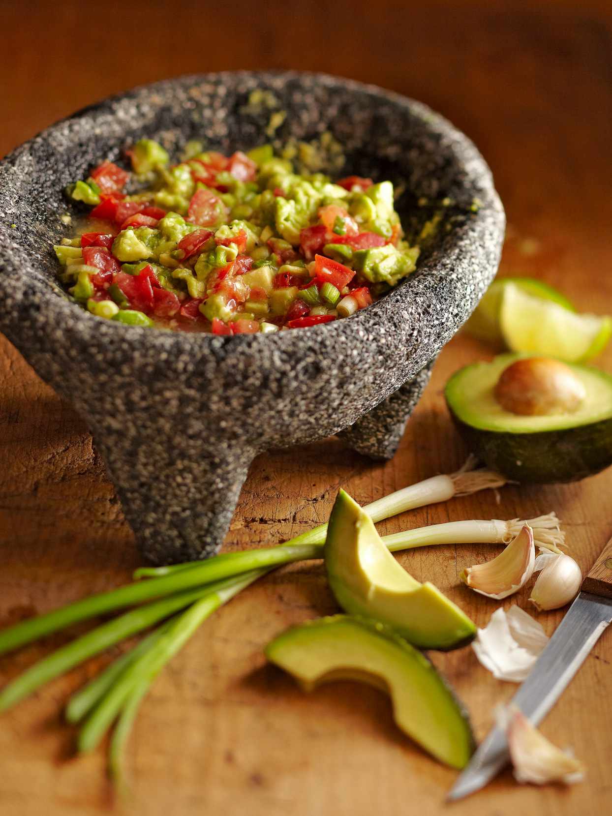Chunky Guacamole in stone bowl with sliced avocados and garlic cloves