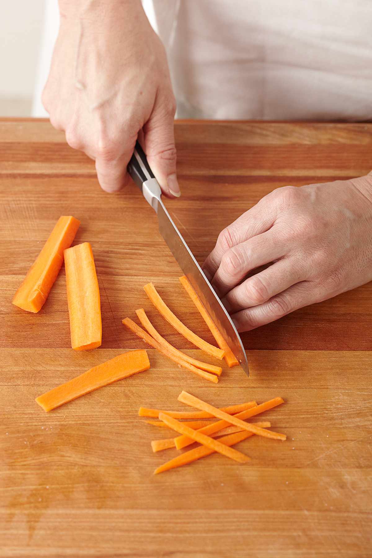 Julienne slicing carrots with knife on cutting board