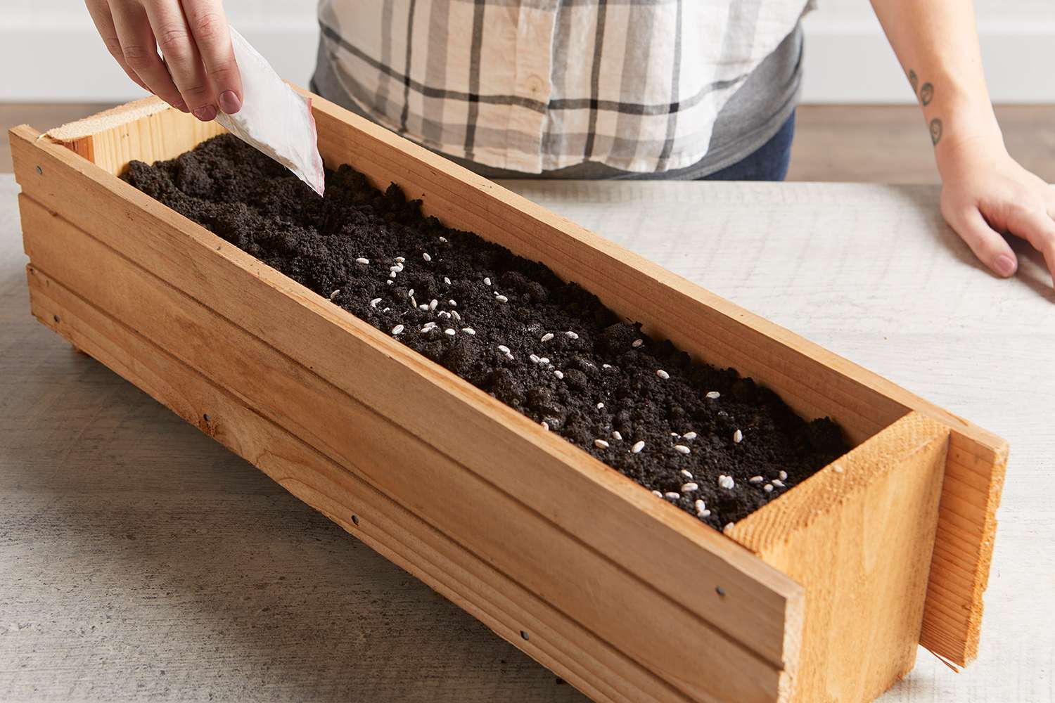 person pouring seeds from bag into wooden planter