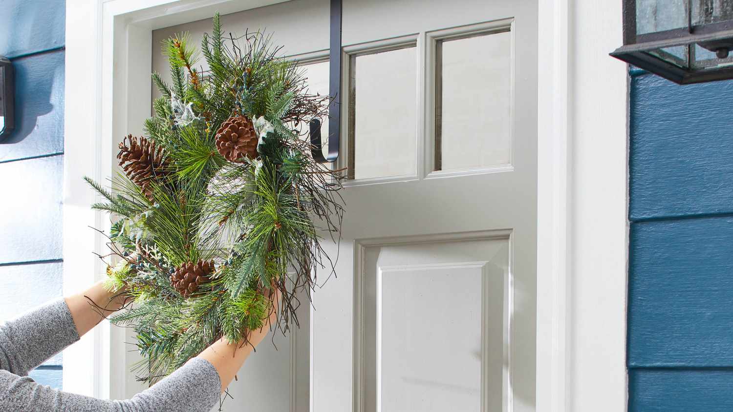 Woman hanging a green evergreen wreath on a gray front door