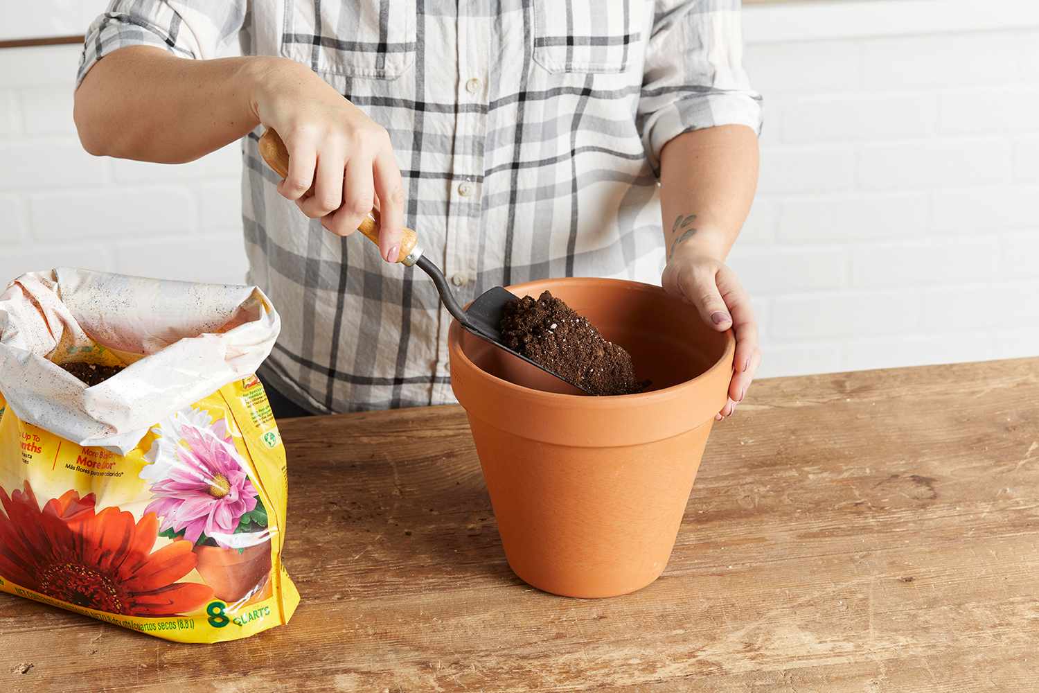 person using shovel to scoop soil from bag into terra cotta pot