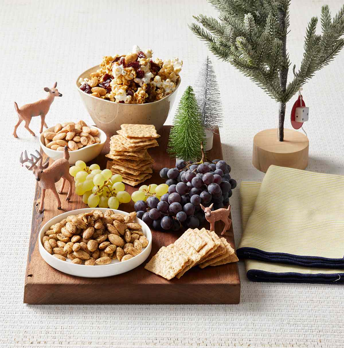 wooden board with grapes crackers snack mix and deer figures and trees