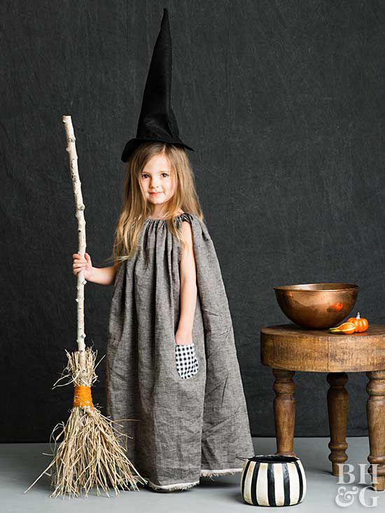 little girl dressed in a homemade halloween costume of a gray dress and black witch hat and witch broom