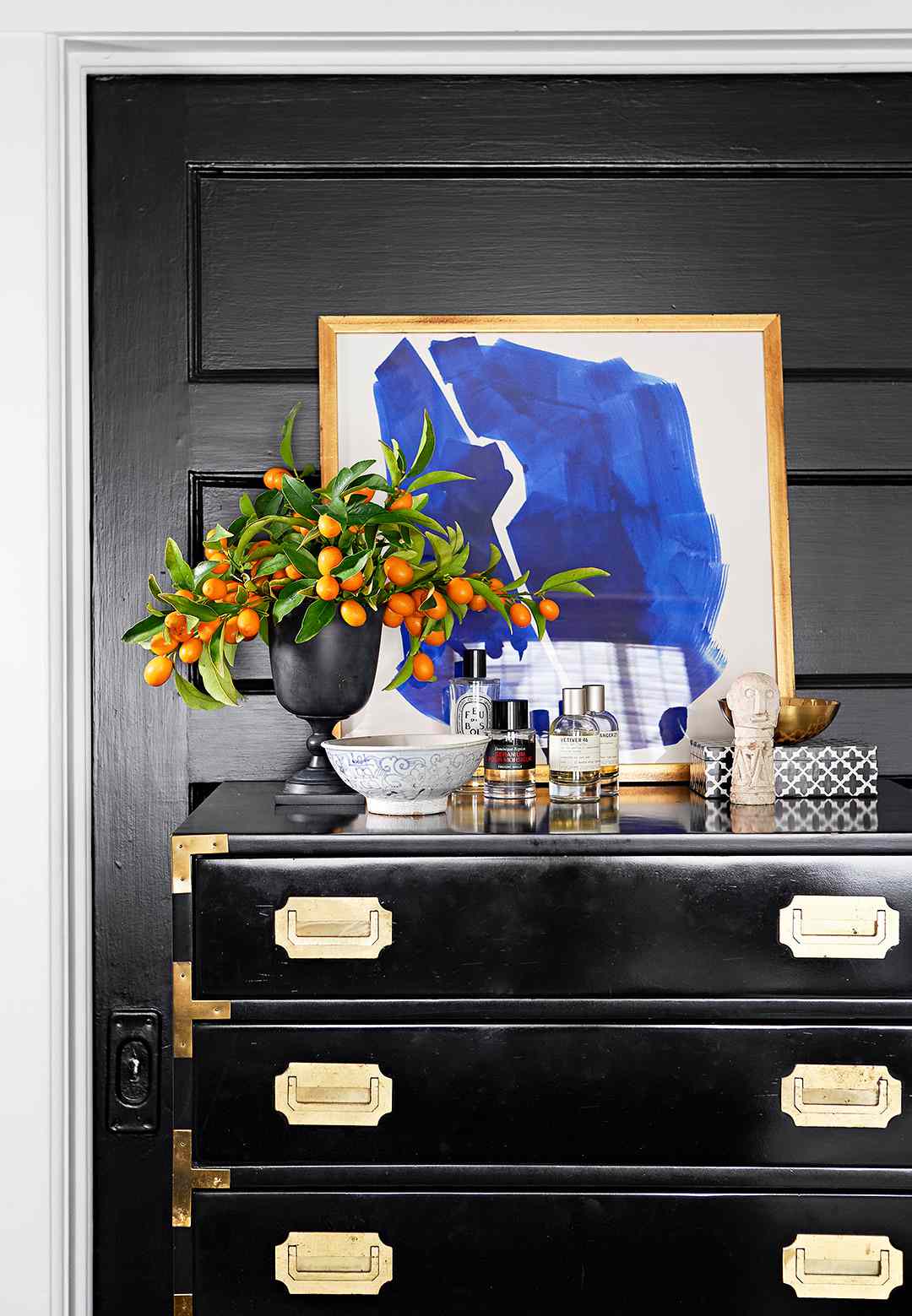 black dresser with gold hardware and dresser-top display of art, cologne bottles