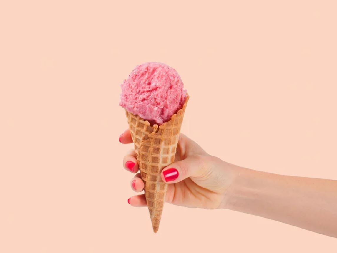 Hand Holding Sugar Cone full of a Scoop of Pink Ice Cream