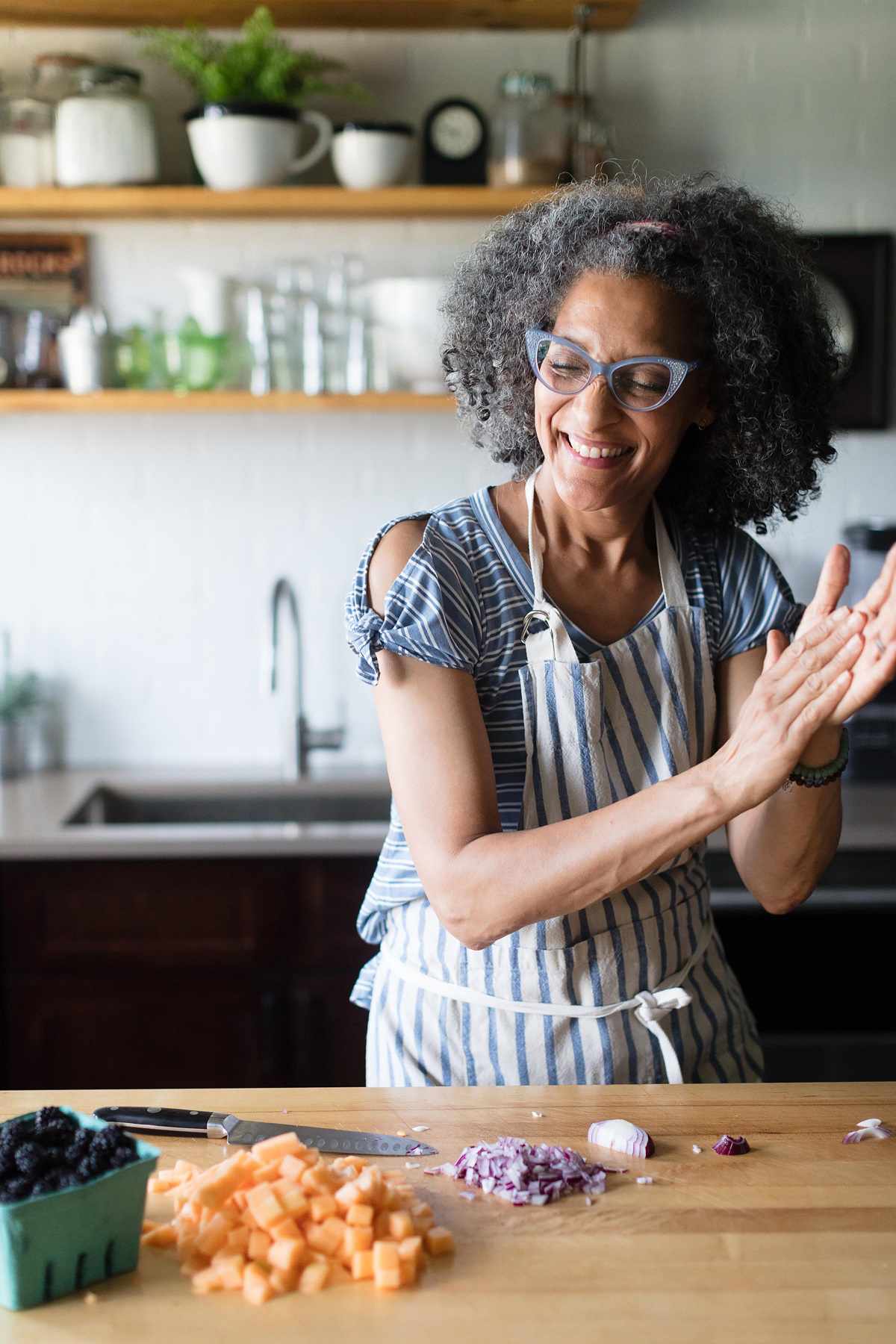 Carla Hall at cutting board laughing and clapping hands