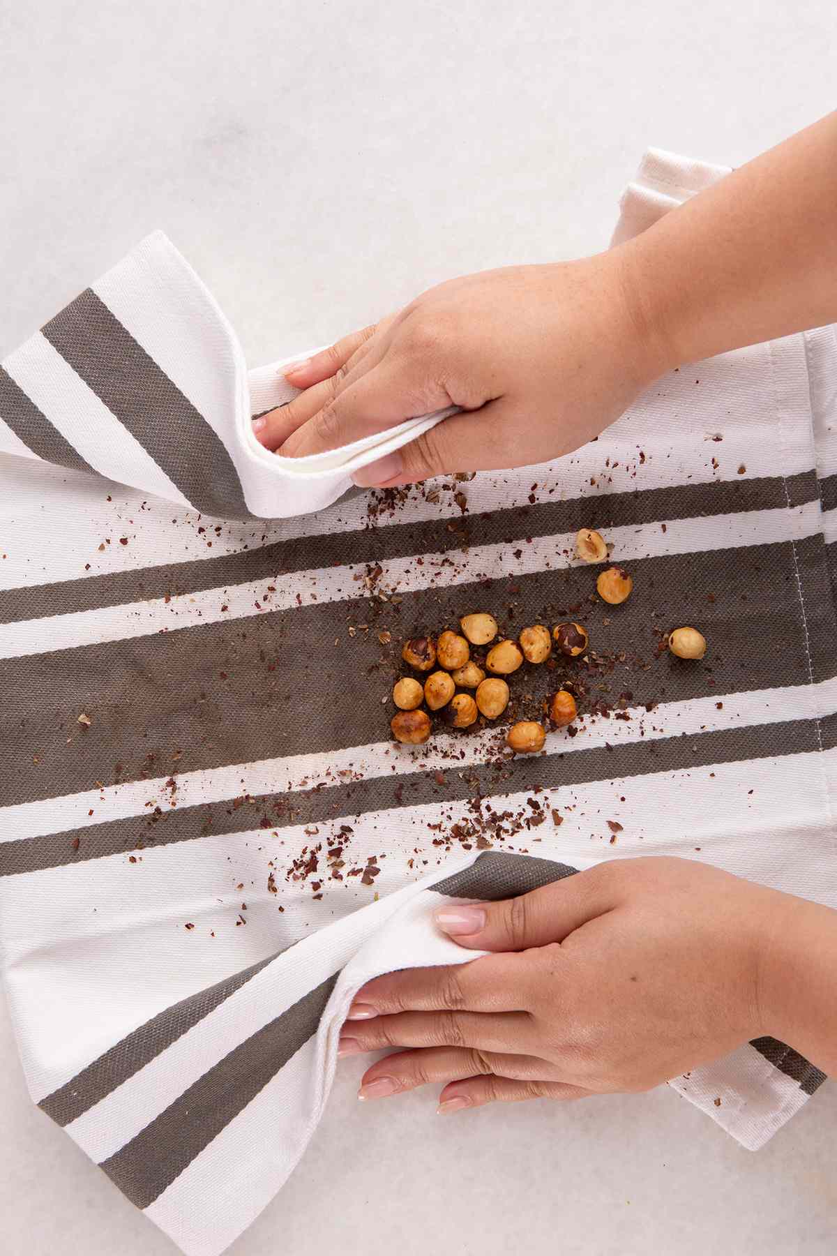 removing skins from hazelnuts on white dish towel with brown stripes